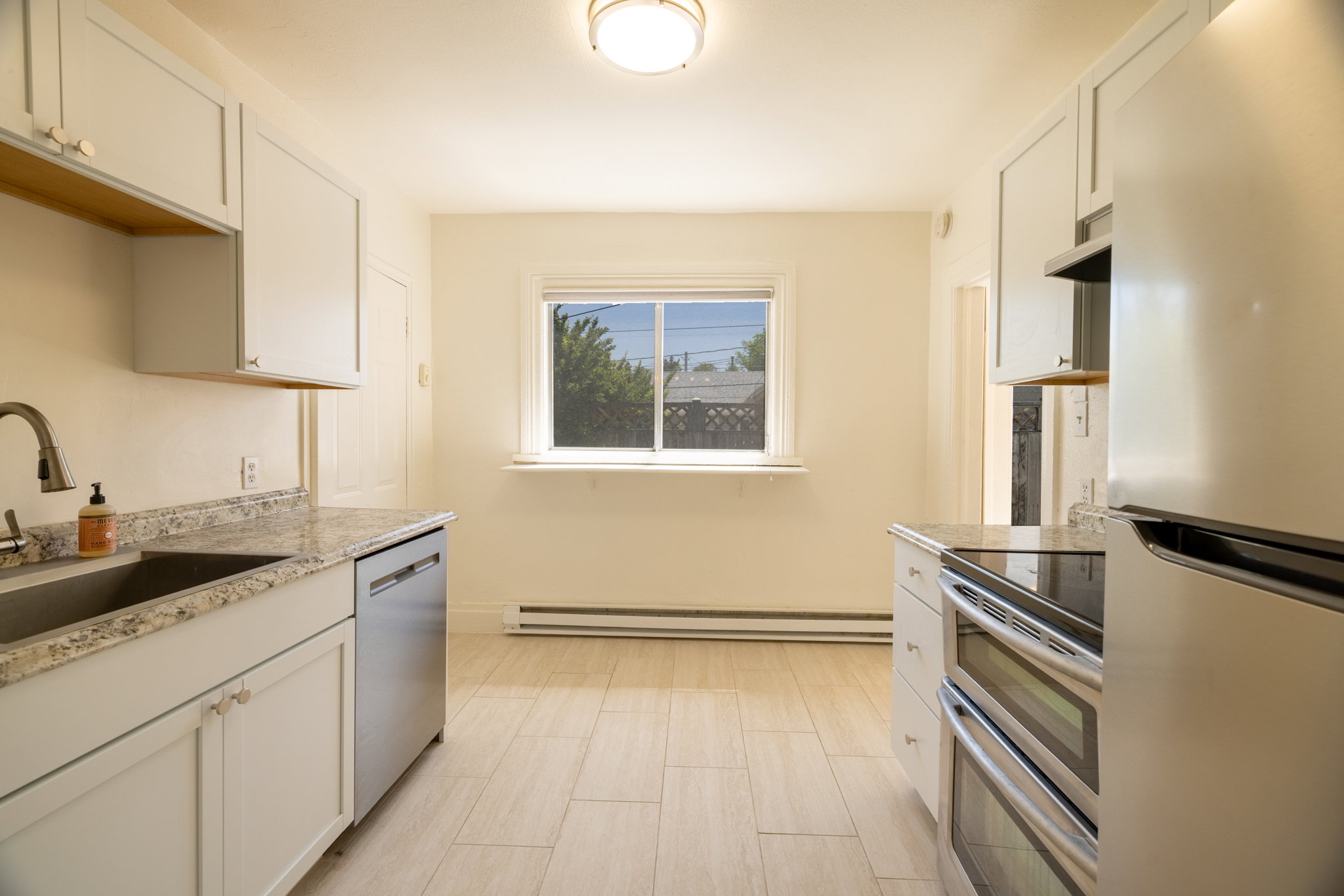 Bright kitchen featuring light-toned cabinetry, light-toned countertops, a stainless steel dishwasher, a double oven range, and wood-finish tile flooring