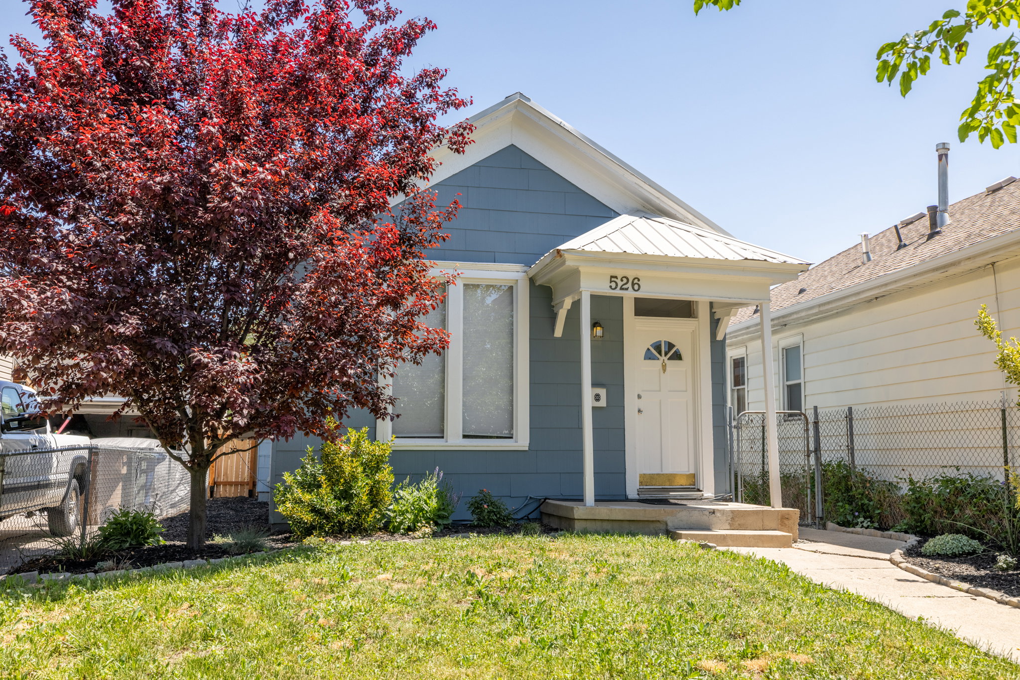 Light blue exterior with white trim, featuring a covered front porch with white columns and a metal roof