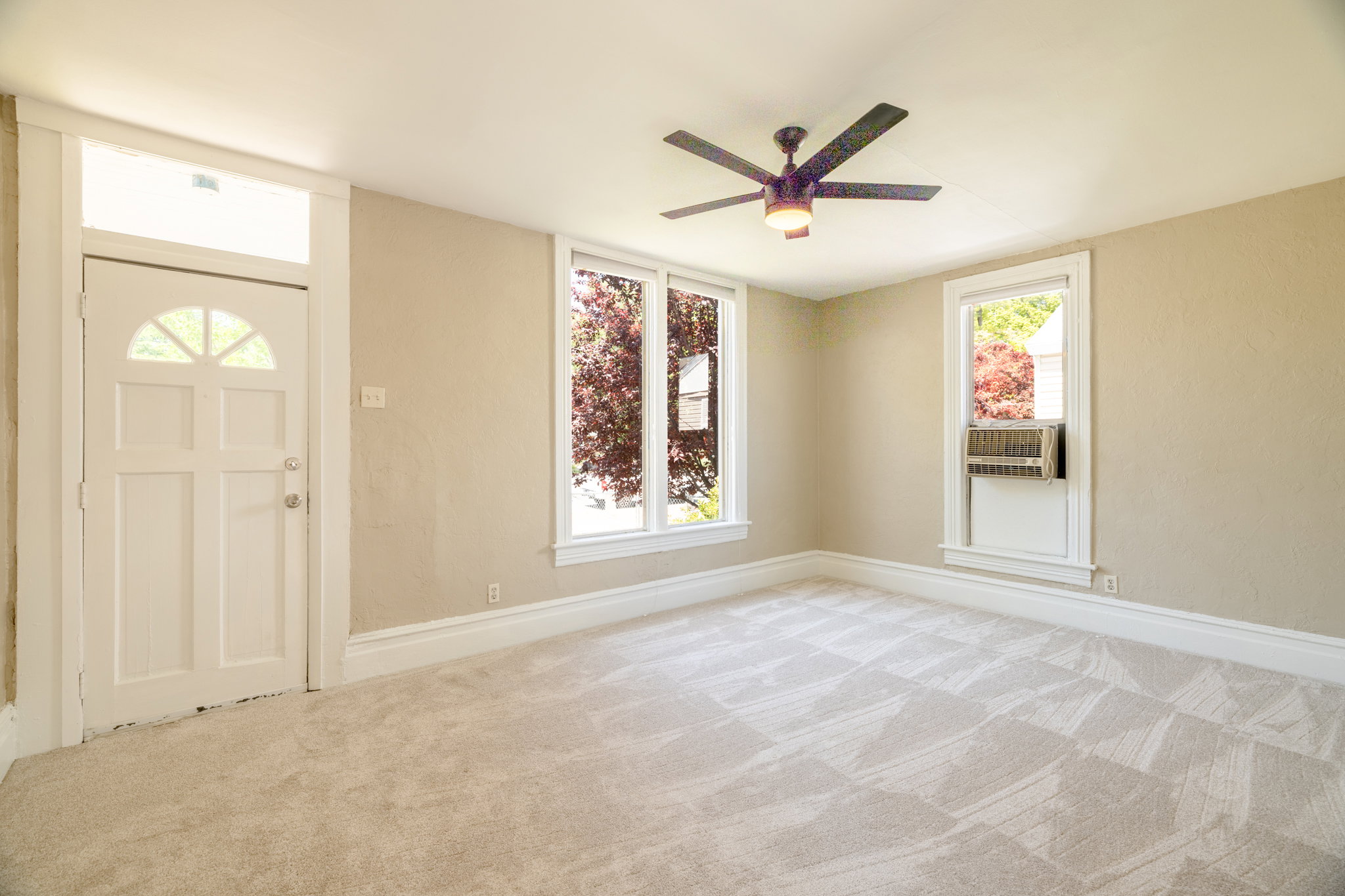 Neutral-toned room featuring patterned carpet, a white paneled door with an arched transom window, and two windows with white trim
