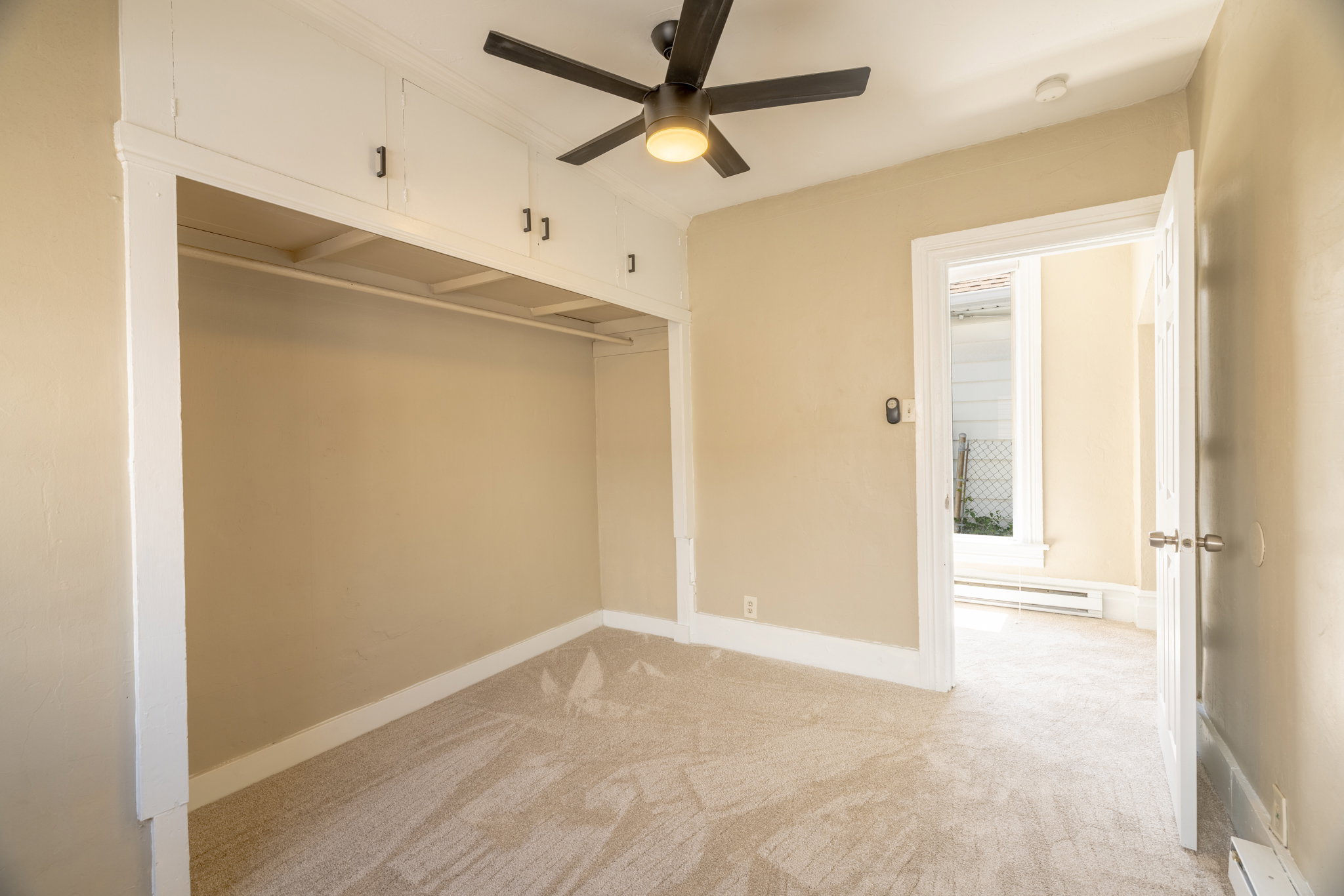 Neutral-toned room featuring wall-to-wall carpeting, a built-in closet with upper cabinetry, and a ceiling fan