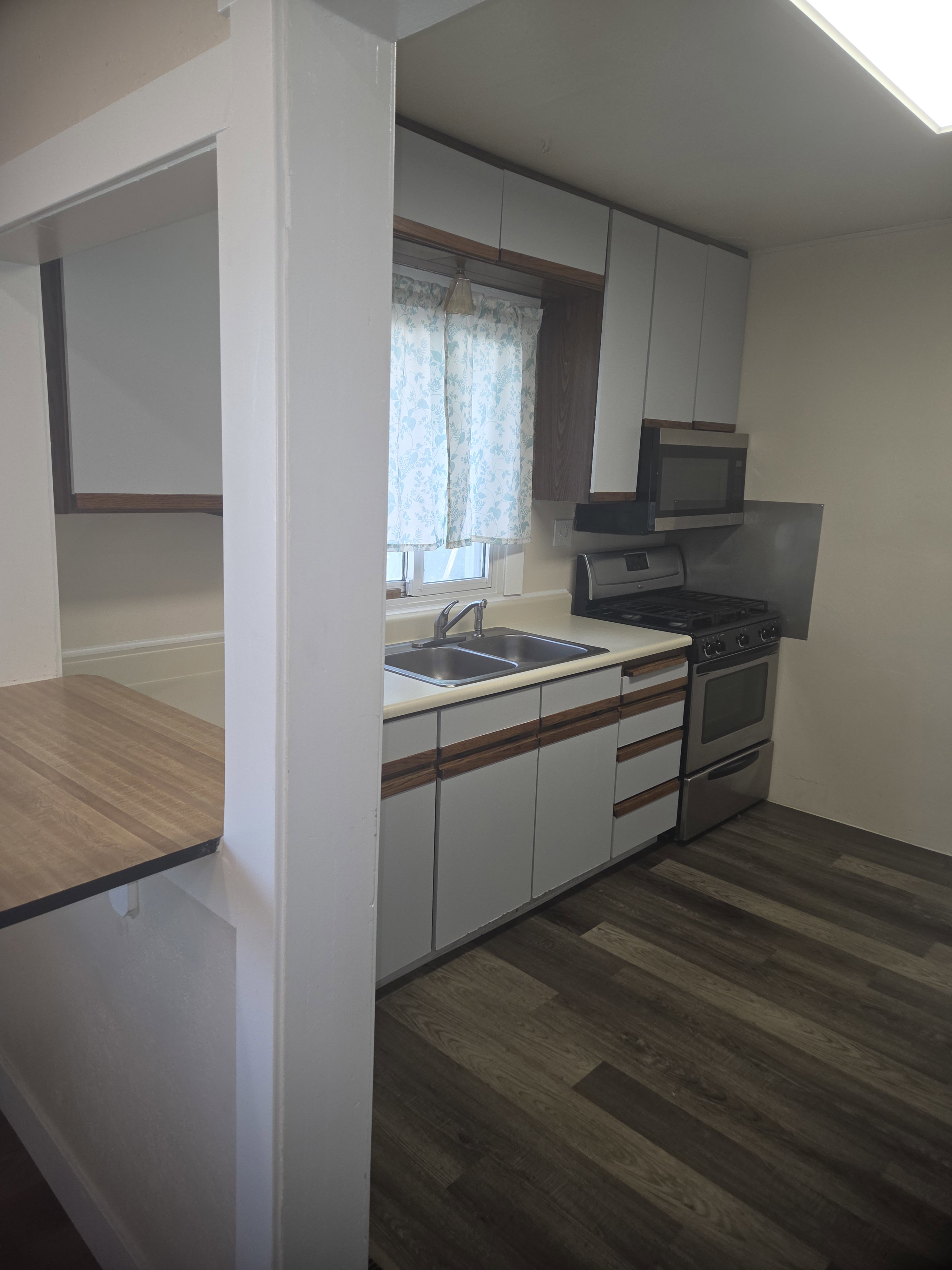 Kitchen featuring wood-finish flooring, white cabinetry with wood accents, double basin stainless steel sink, stainless steel gas range, and a built-in microwave