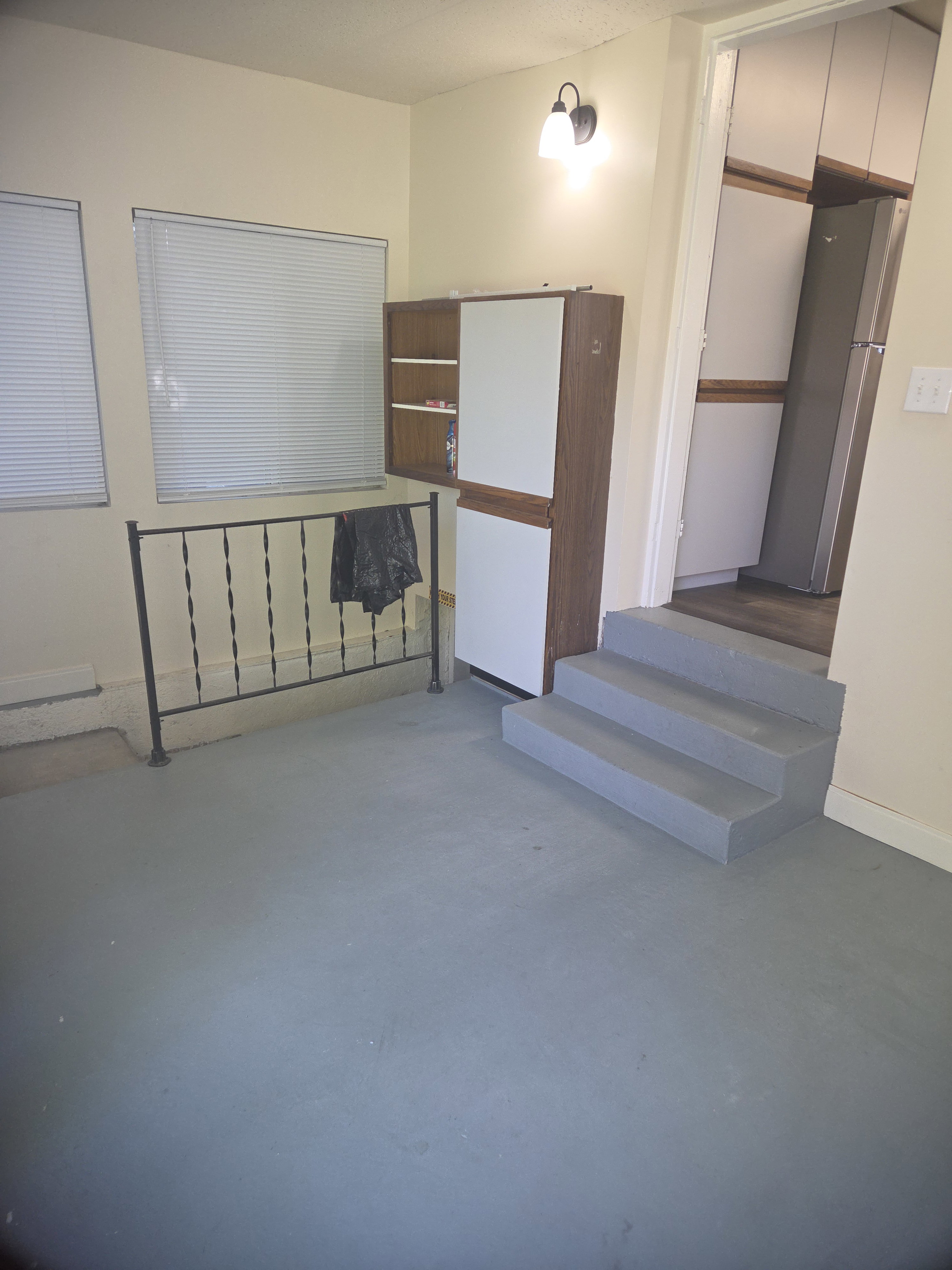 Multi-purpose room featuring two windows with horizontal blinds, a black wrought iron railing, and a built-in cabinetry unit with wood-finish and white panels