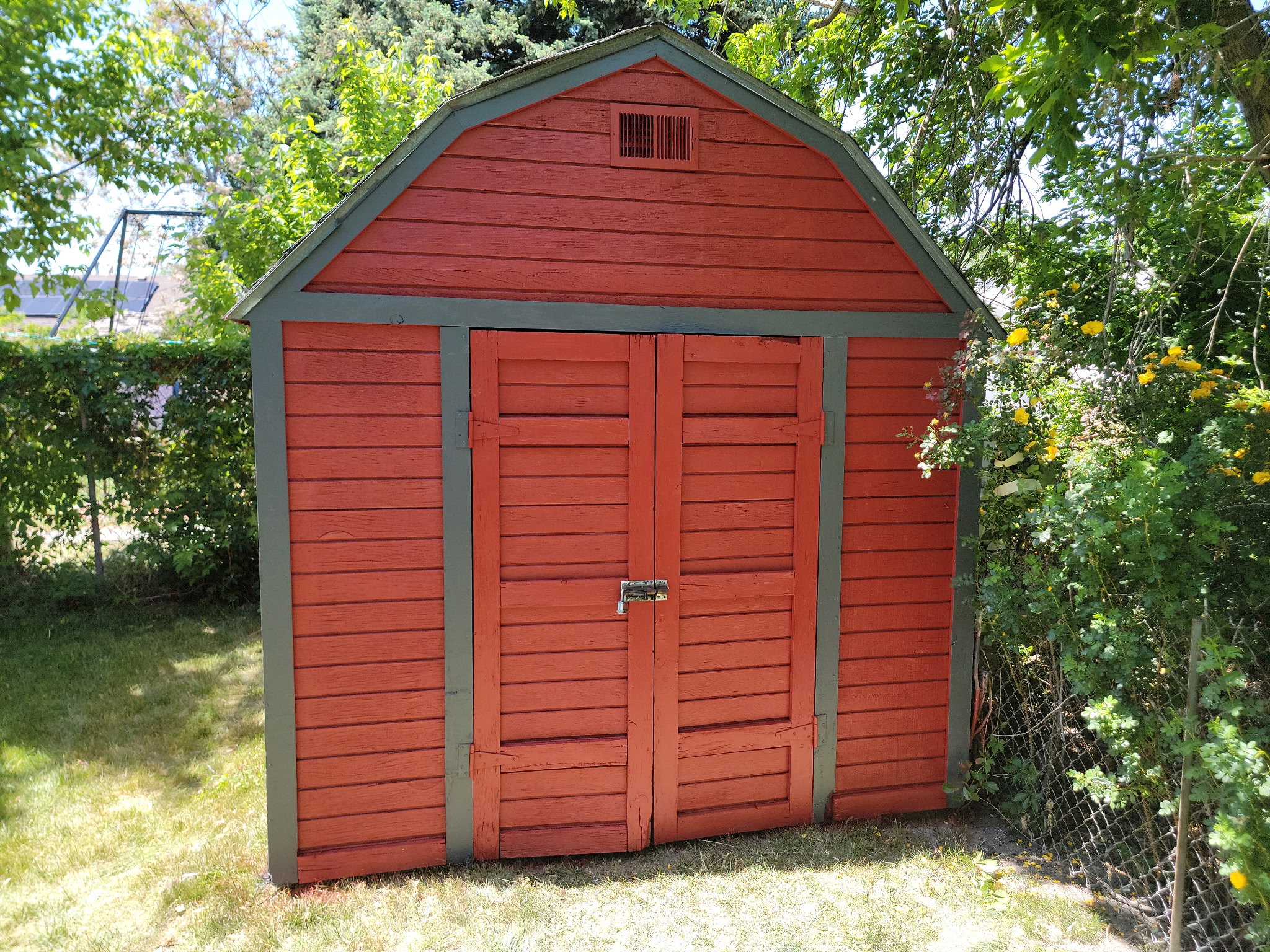 Red storage shed featuring a gambrel roof and double louvered doors