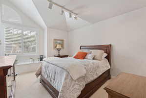 Vaulted ceiling room featuring a large window with plantation shutters, an arched transom window, and track lighting