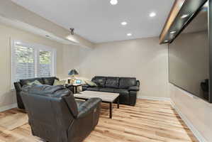 Spacious lounge with wall television featuring wood-finish flooring, recessed ceiling lighting, and a window with plantation shutters