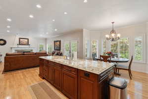 Kitchen island with granite countertop and integrated sink, hardwood flooring, recessed lighting, and a breakfast area with multiple windows featuring plantation shutters