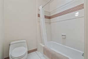 Full bathroom featuring a white tile shower surround with a decorative accent band, a white bathtub, and a modern white toilet