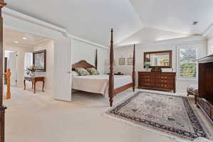 Expansive bedroom featuring vaulted ceilings, light-colored carpeting, and plantation shutters
