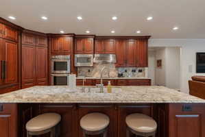 Kitchen featuring a large island with granite countertop, mahogany wood cabinetry, stainless steel Thermador double ovens, stainless steel microwave, and integrated refrigerator and dishwasher