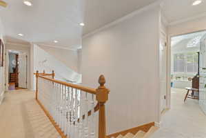 Upper-level landing featuring light-toned carpeting, crown molding, recessed lighting, and a wood-finish handrail with white balusters
