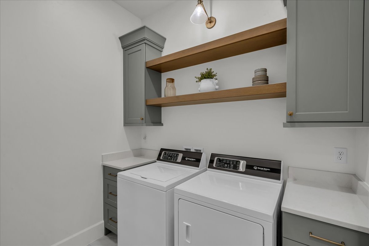 Laundry area featuring light gray cabinetry, wood-finish open shelving, and white countertops