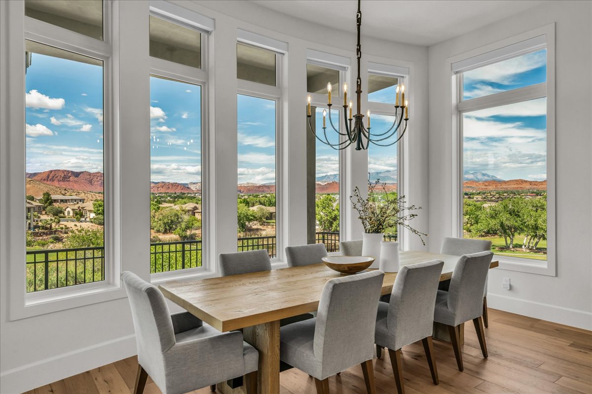 Dining area featuring abundant natural light from multiple tall windows, a wrought iron chandelier, hardwood flooring, and distant mountain scenery