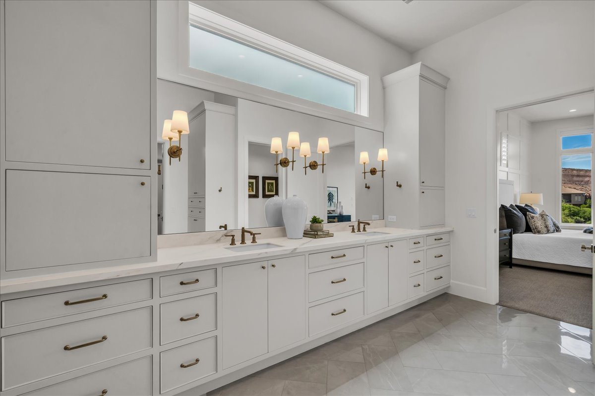 Primary bathroom: dual vanity with integrated sinks, expansive mirror, and sconce lighting