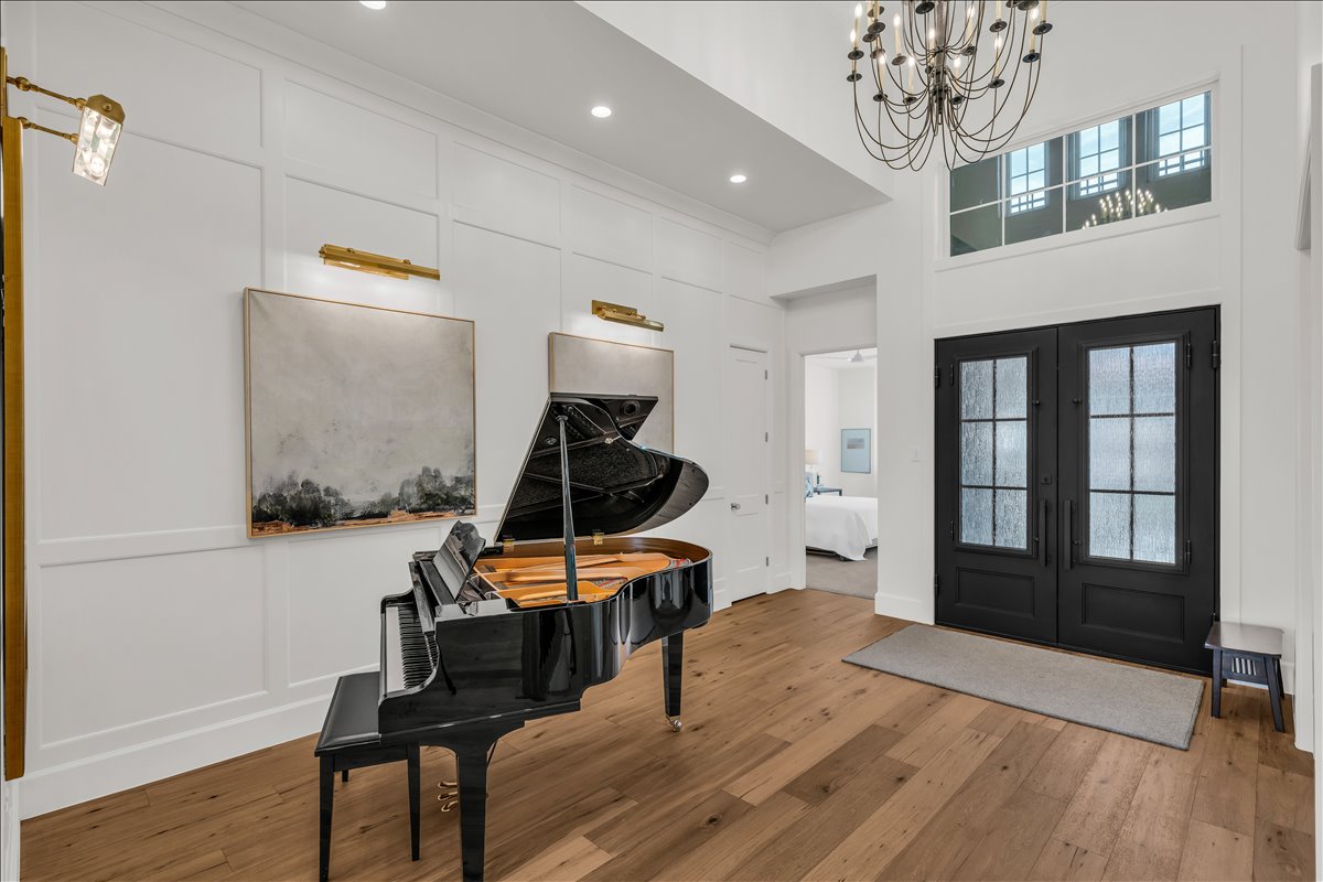 Grand foyer entry featuring double front doors with textured glass, expansive wood-finish flooring, and a two-story ceiling with a chandelier