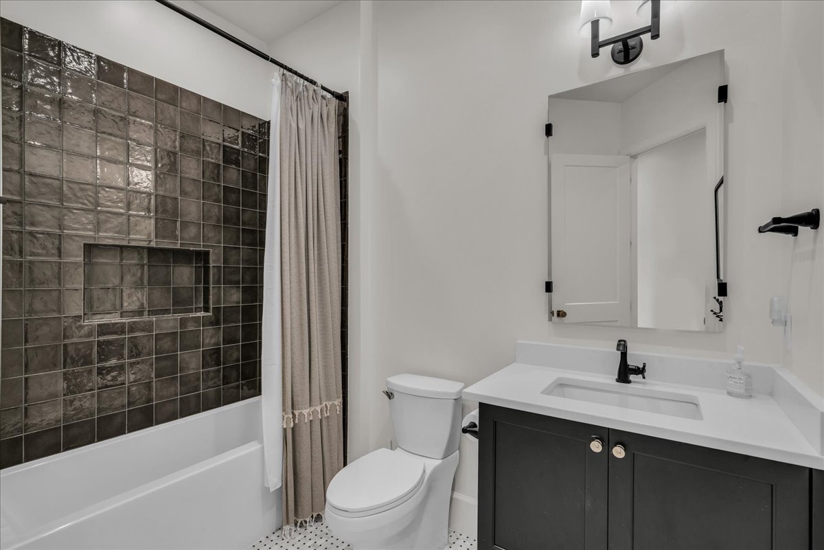 Bathroom featuring a dark tiled tub/shower combination with an integrated niche, a white vanity with an undermount sink and matte black faucet, a framed mirror, and hexagonal floor tiling