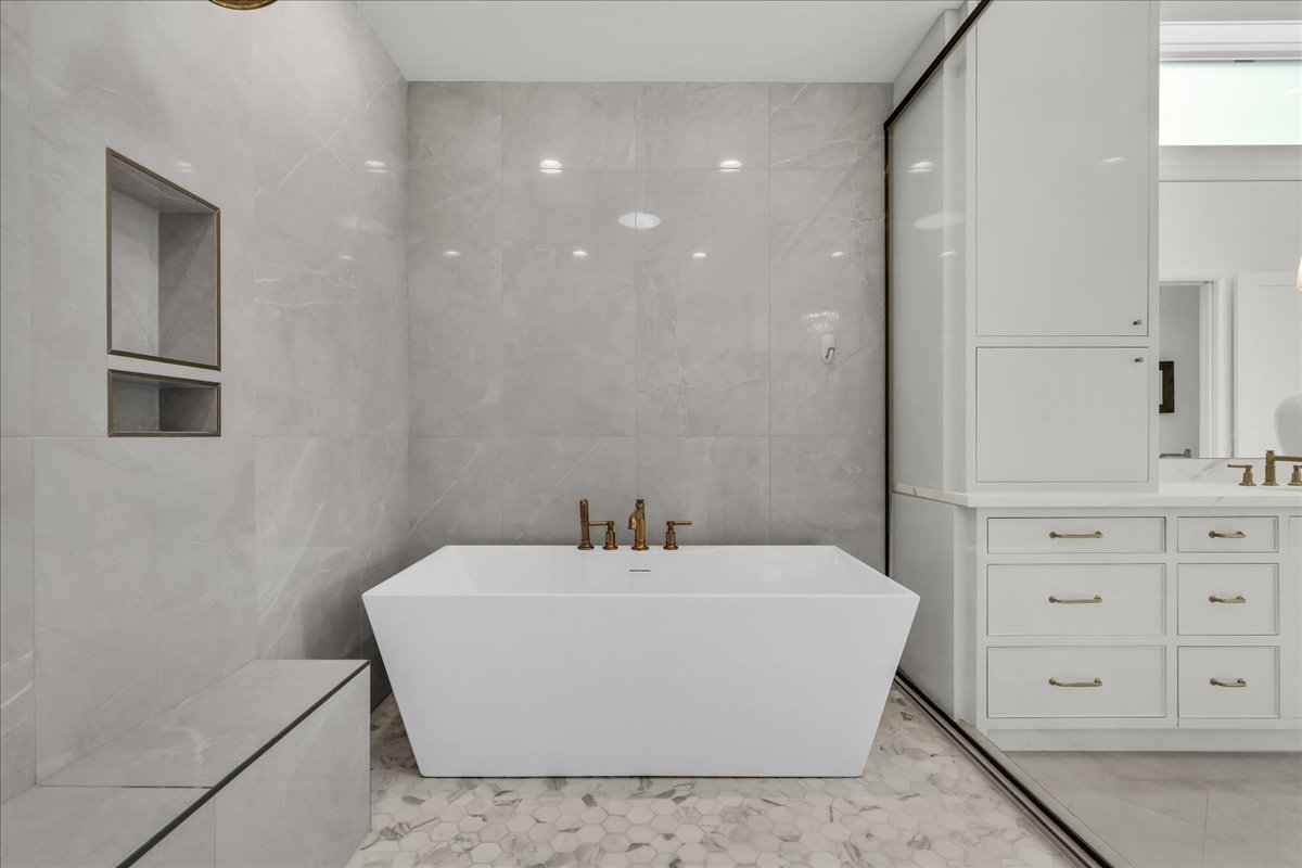 Primary bathroom: freestanding soaking tub with brass fixtures, set against large format wall tiling and hexagonal floor tiling