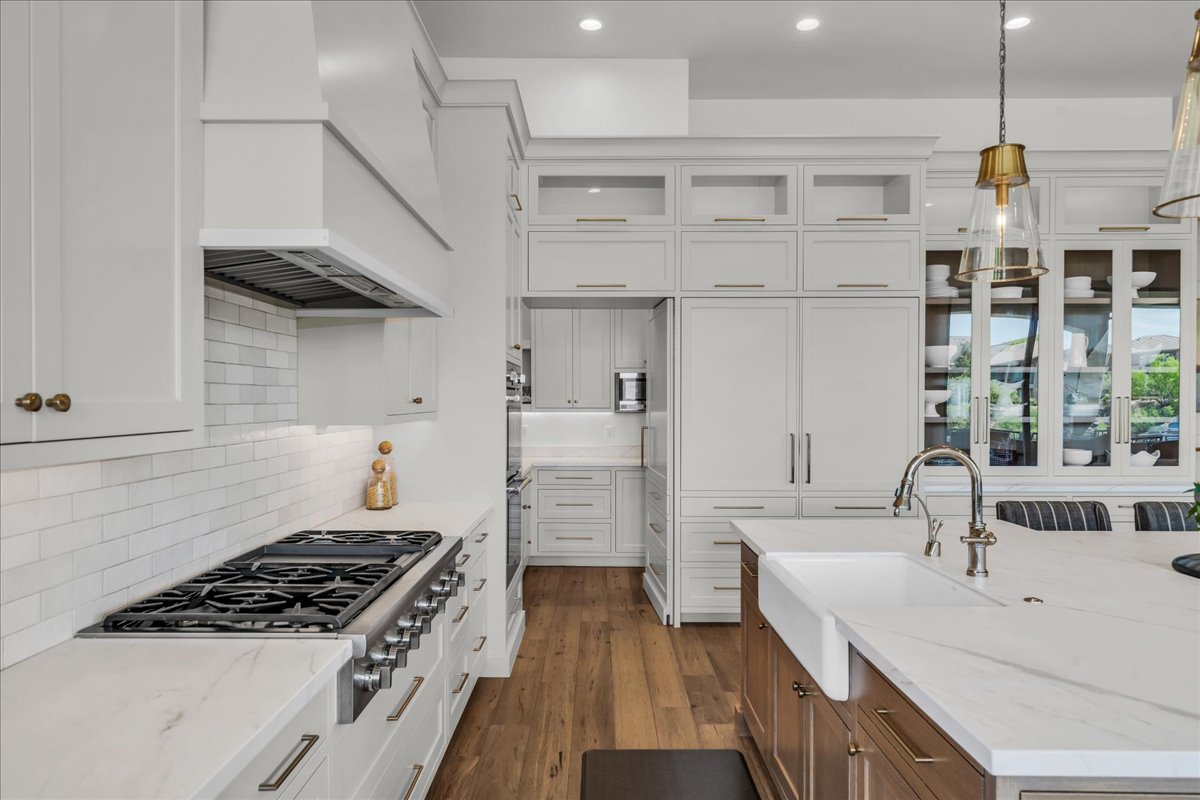 Gourmet kitchen with professional-grade gas range, full-height subway tile backsplash, white shaker cabinetry, integrated refrigerator, and a kitchen island featuring a farmhouse sink and polished chrome faucet