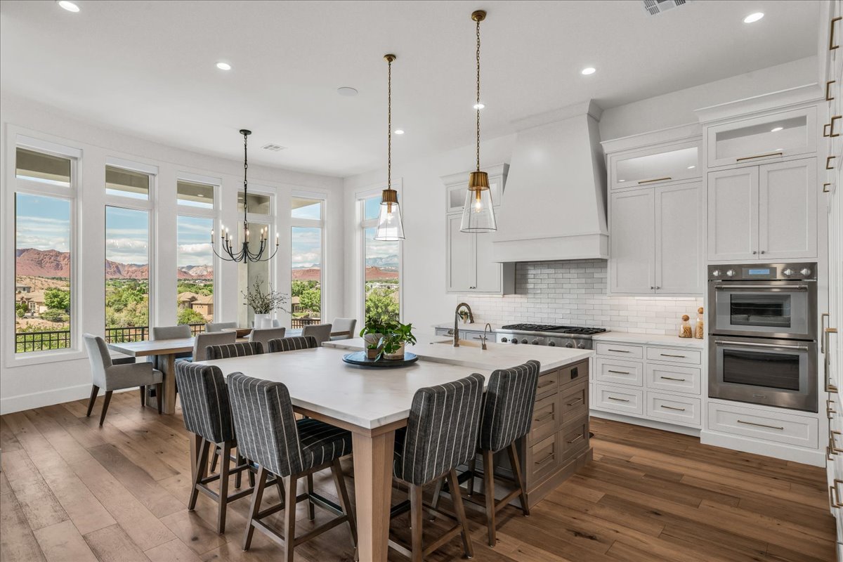 Gourmet kitchen featuring a large central island, white shaker cabinetry, stainless steel appliances, and wood-finish flooring