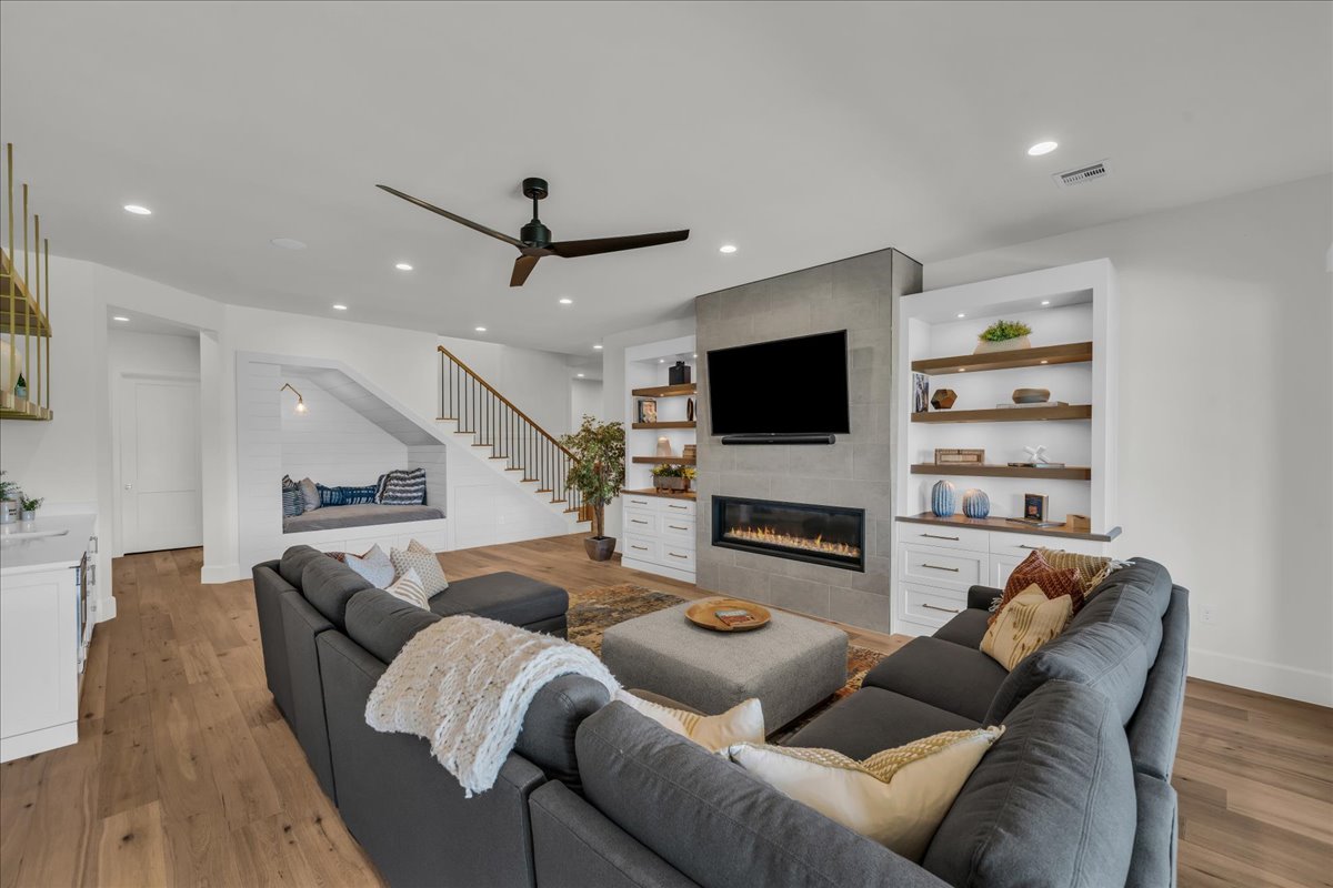 Living area showcasing wood-finish flooring, a contemporary fireplace with a stone surround, and built-in shelving