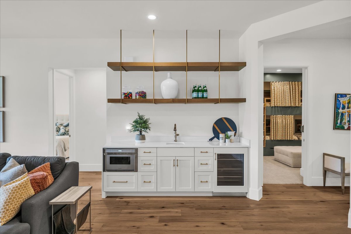 Built-in beverage station featuring white cabinetry, a quartz countertop, integrated microwave, beverage cooler, and open shelving with brass hardware