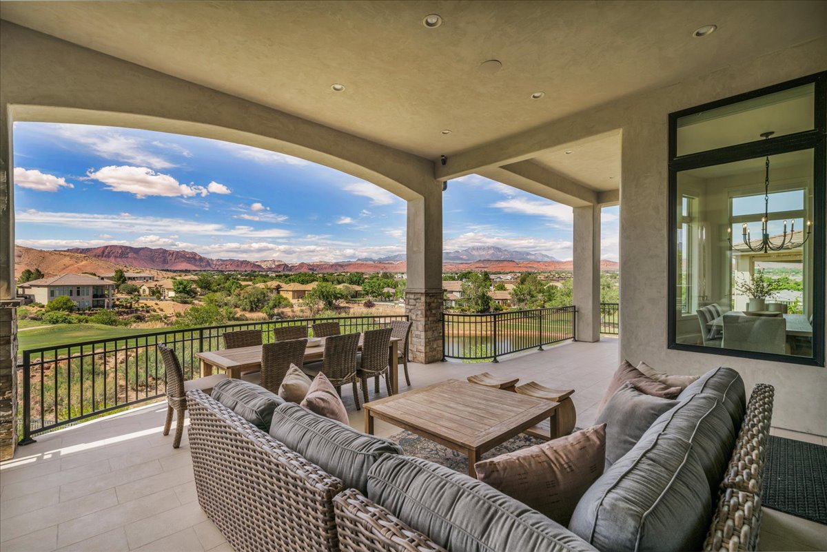Expansive covered patio featuring a tiled floor, stone-clad pillars, and a black wrought iron railing