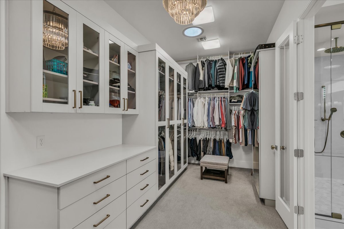 Spacious primary closet featuring custom cabinetry, integrated shelving, and glass-front upper storage
