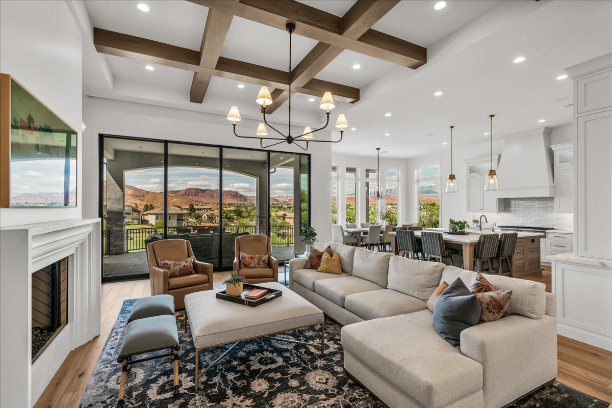 Spacious living area featuring exposed wood-finish ceiling beams, expansive black-framed glass sliding doors, and a white mantel fireplace