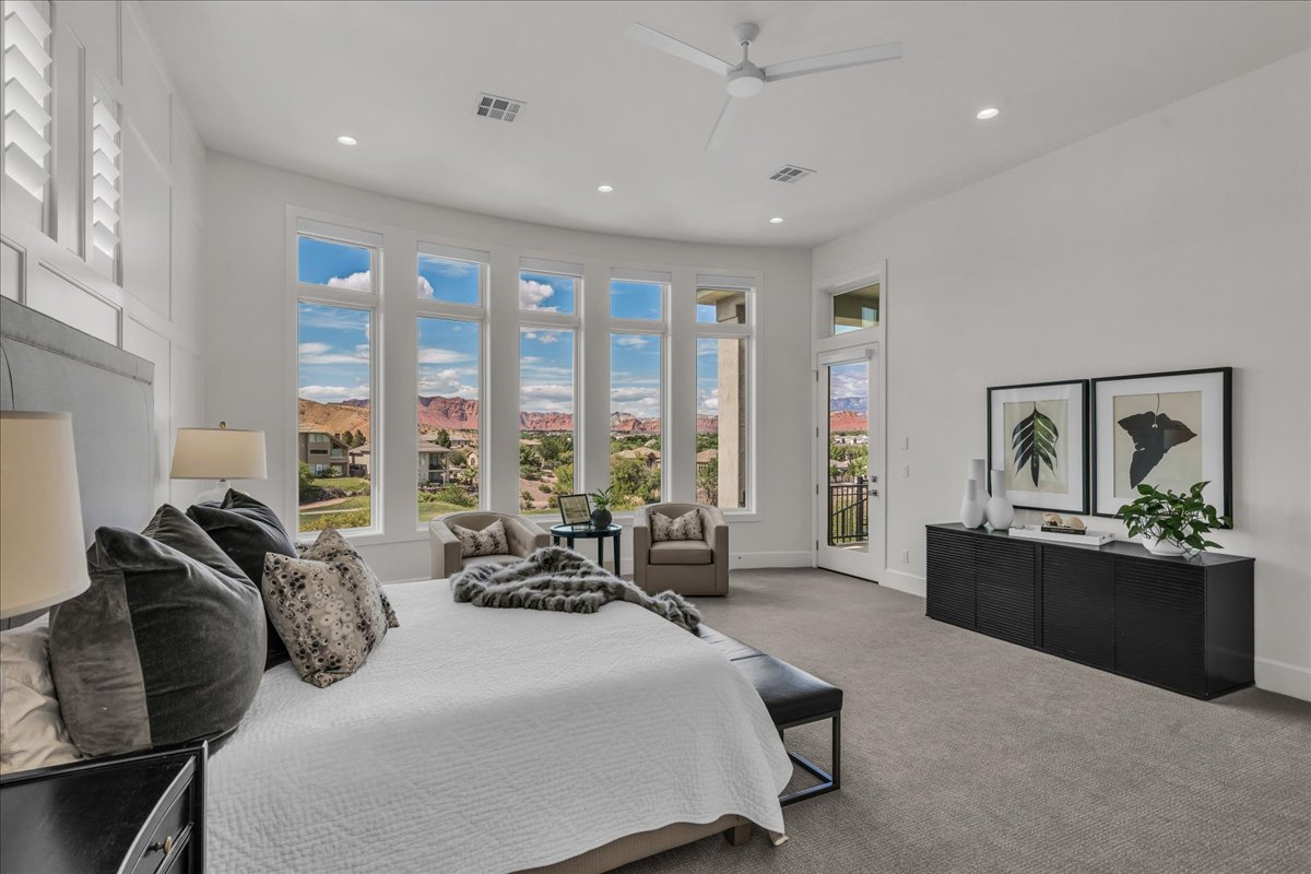Primary bedroom with full-height windows with a curved design, white shaker shutters, a private balcony, recessed lighting, and a ceiling fan