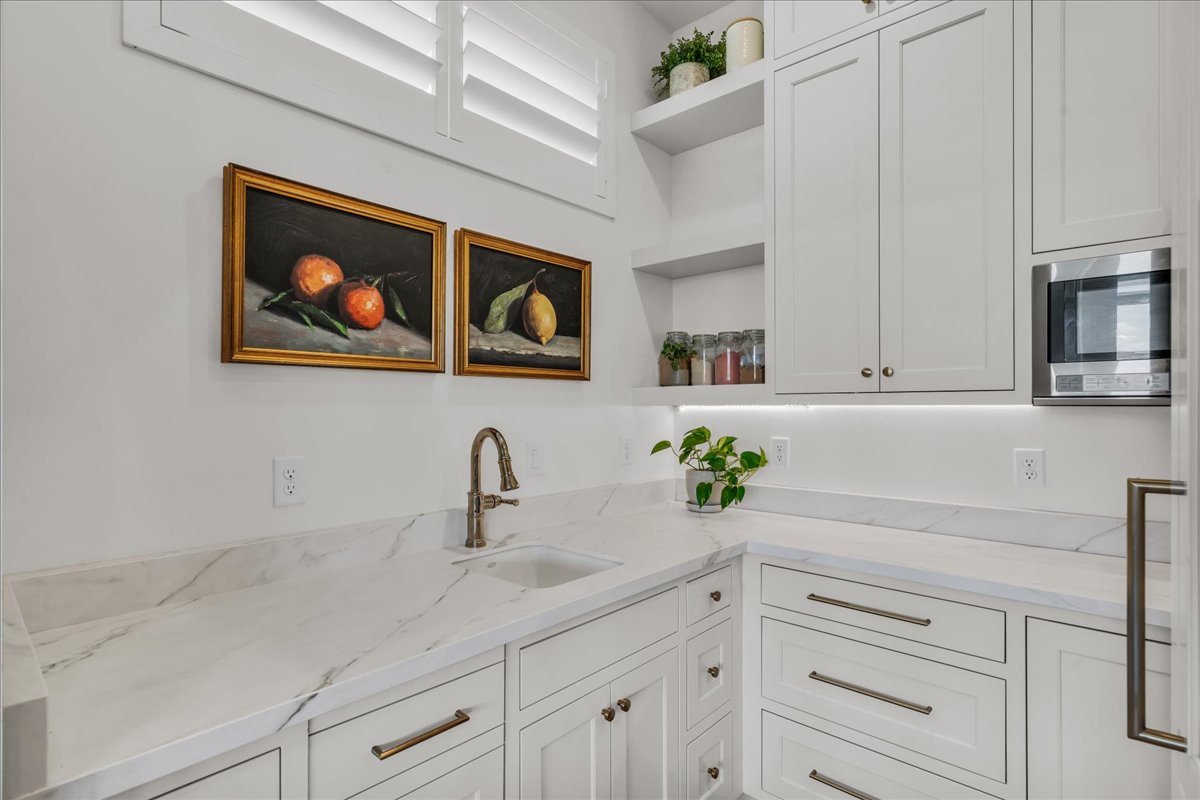 White shaker cabinetry with brass hardware, marble-look countertops, and an undermount sink with a bronze-finish faucet