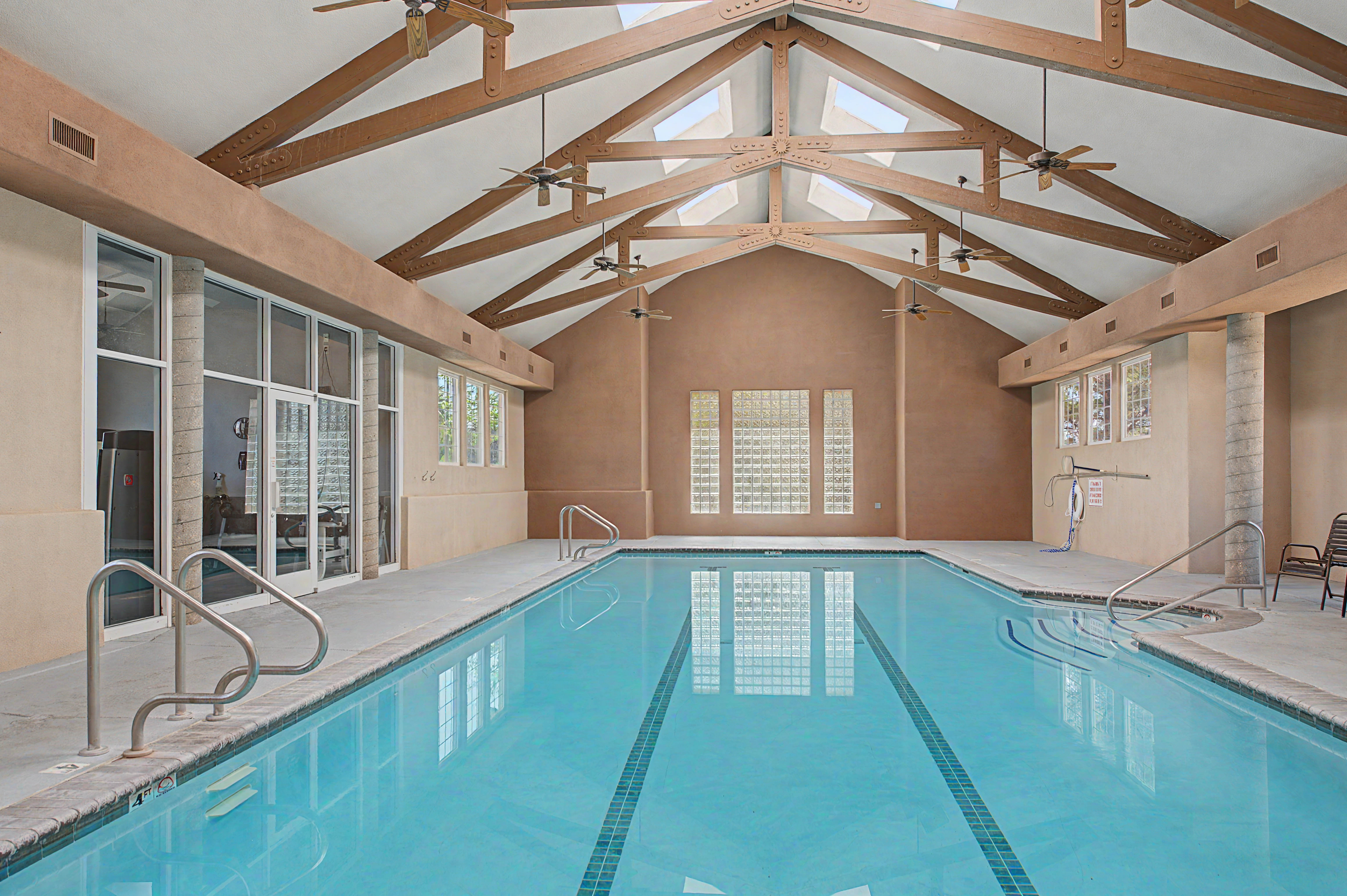 Indoor swimming pool featuring an exposed beam vaulted ceiling with skylights and ceiling fans