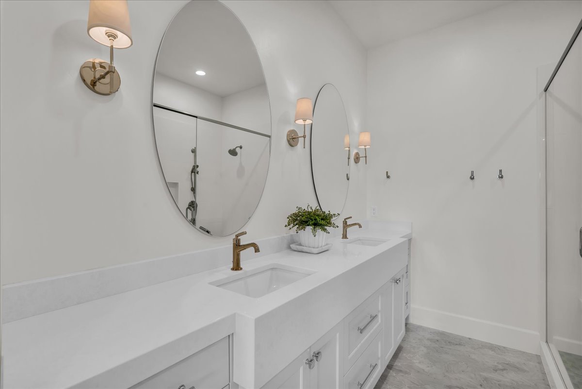 Double vanity featuring white shaker cabinetry, white countertops, and dual oval mirrors