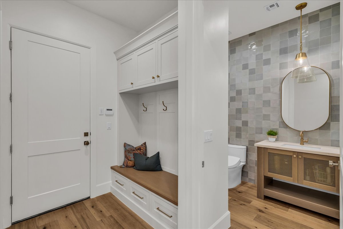 Entryway featuring wood-finish flooring, a white paneled door, and built-in storage with a bench seat and brass hardware