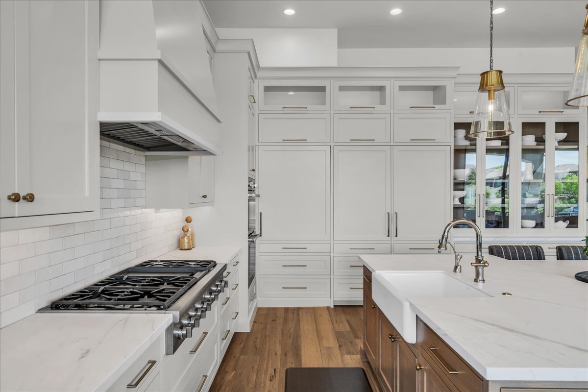 Gourmet kitchen featuring a professional-grade gas range, custom range hood, white subway tile backsplash, integrated paneled appliances, and an oversized island with a farmhouse sink
