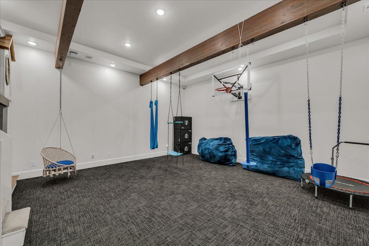 Spacious playroom featuring exposed ceiling beams, recessed lighting, and patterned carpet flooring