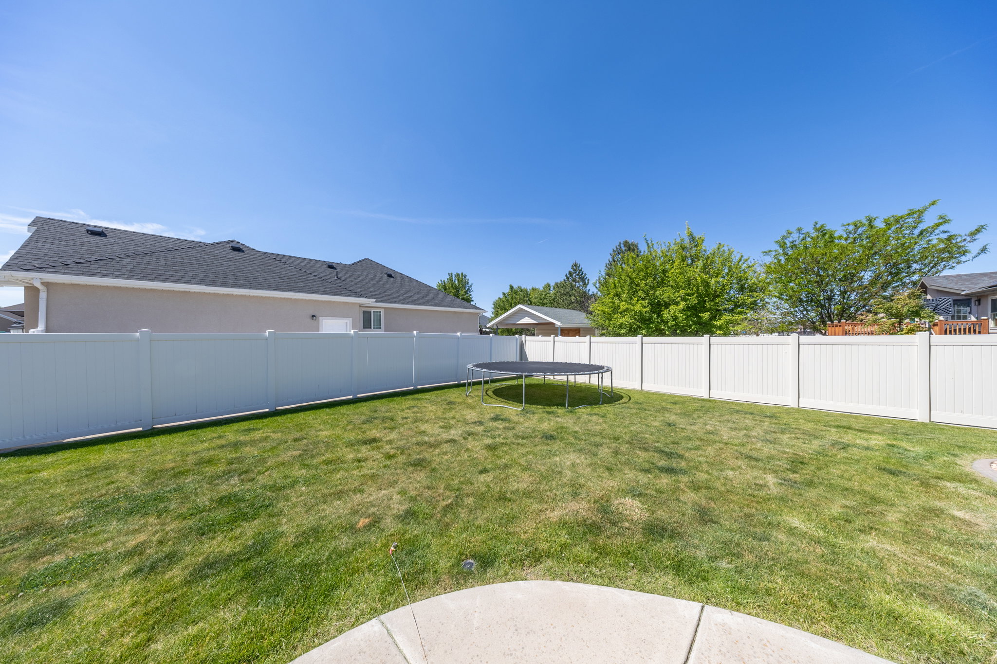 Expansive backyard featuring a manicured lawn, full perimeter white vinyl fencing, and a concrete patio section