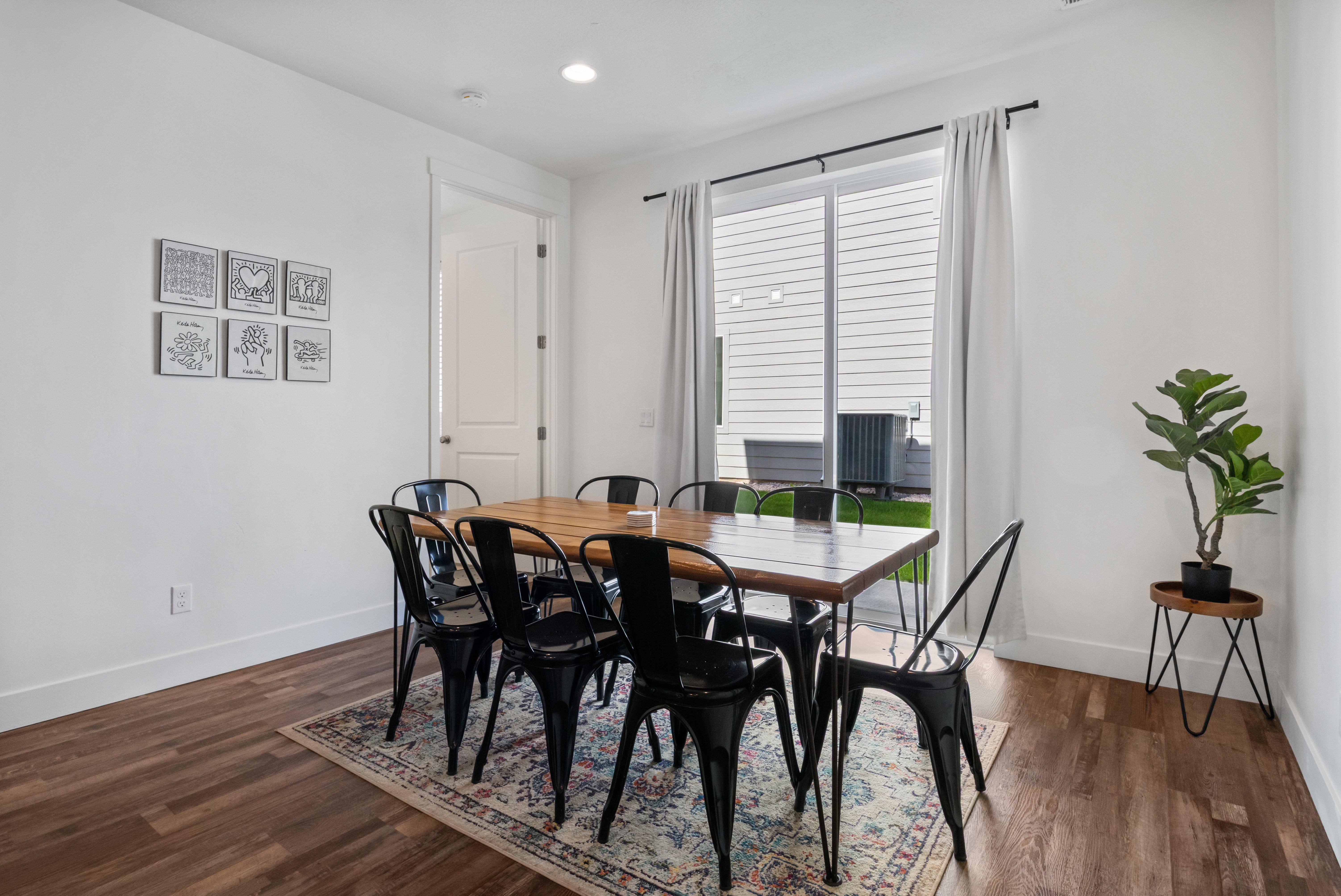 Bright dining area featuring wood-finish flooring, white baseboards, and a sliding glass door with white curtains