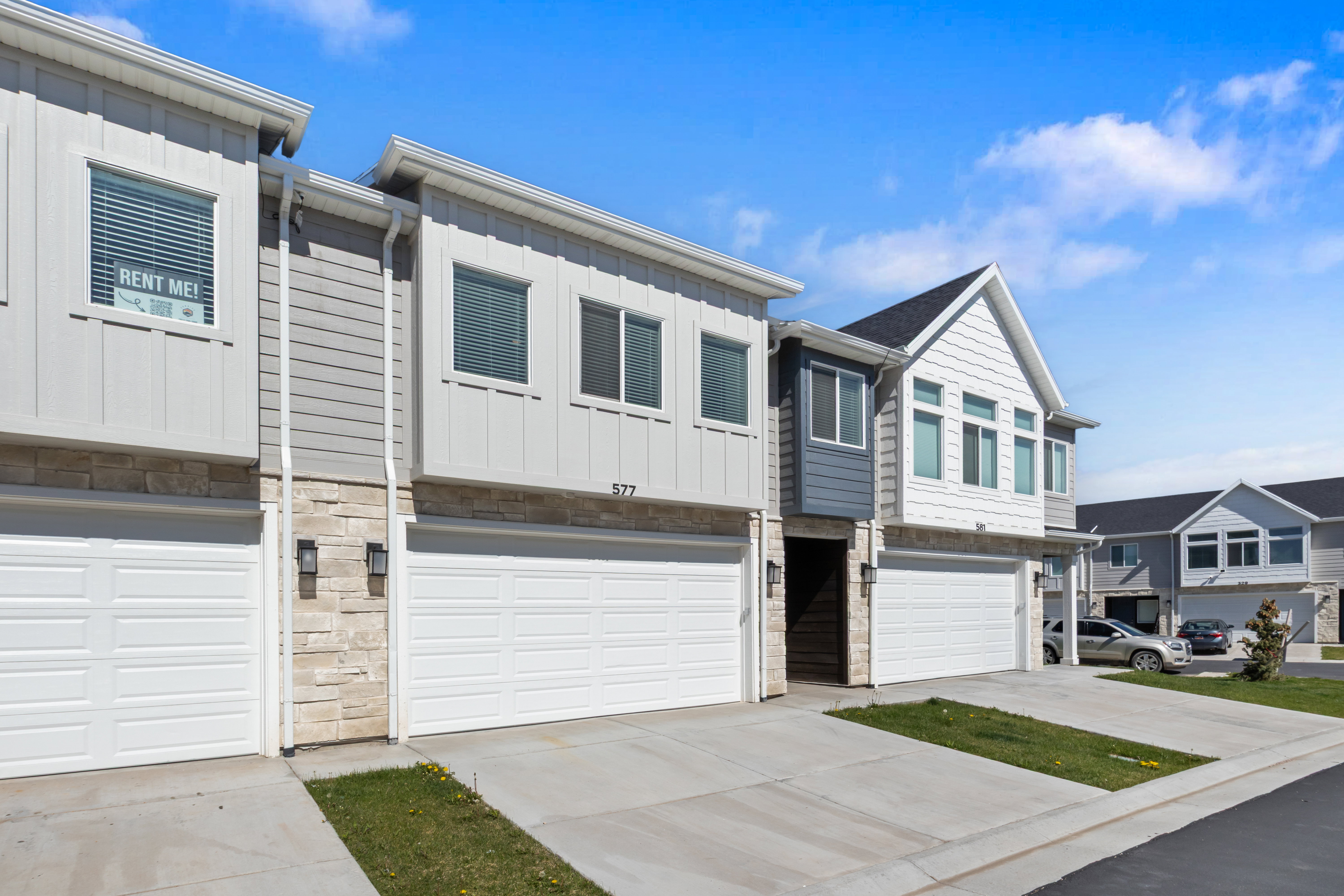 Contemporary townhome exterior featuring stone accents, vertical and horizontal siding, and multiple windows with blinds