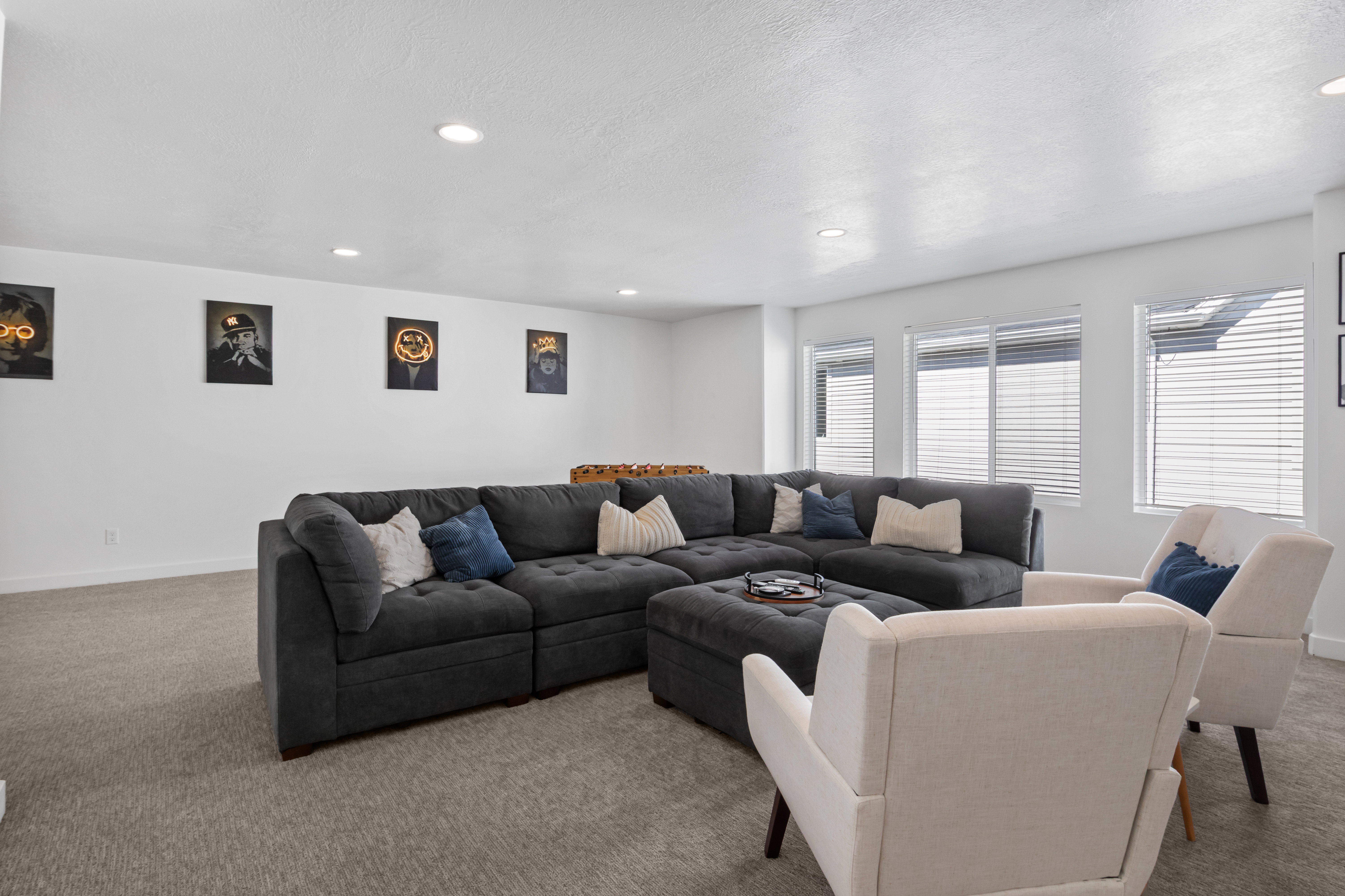 Spacious open-concept room featuring neutral-toned carpeting, recessed ceiling lighting, and multiple windows with horizontal blinds