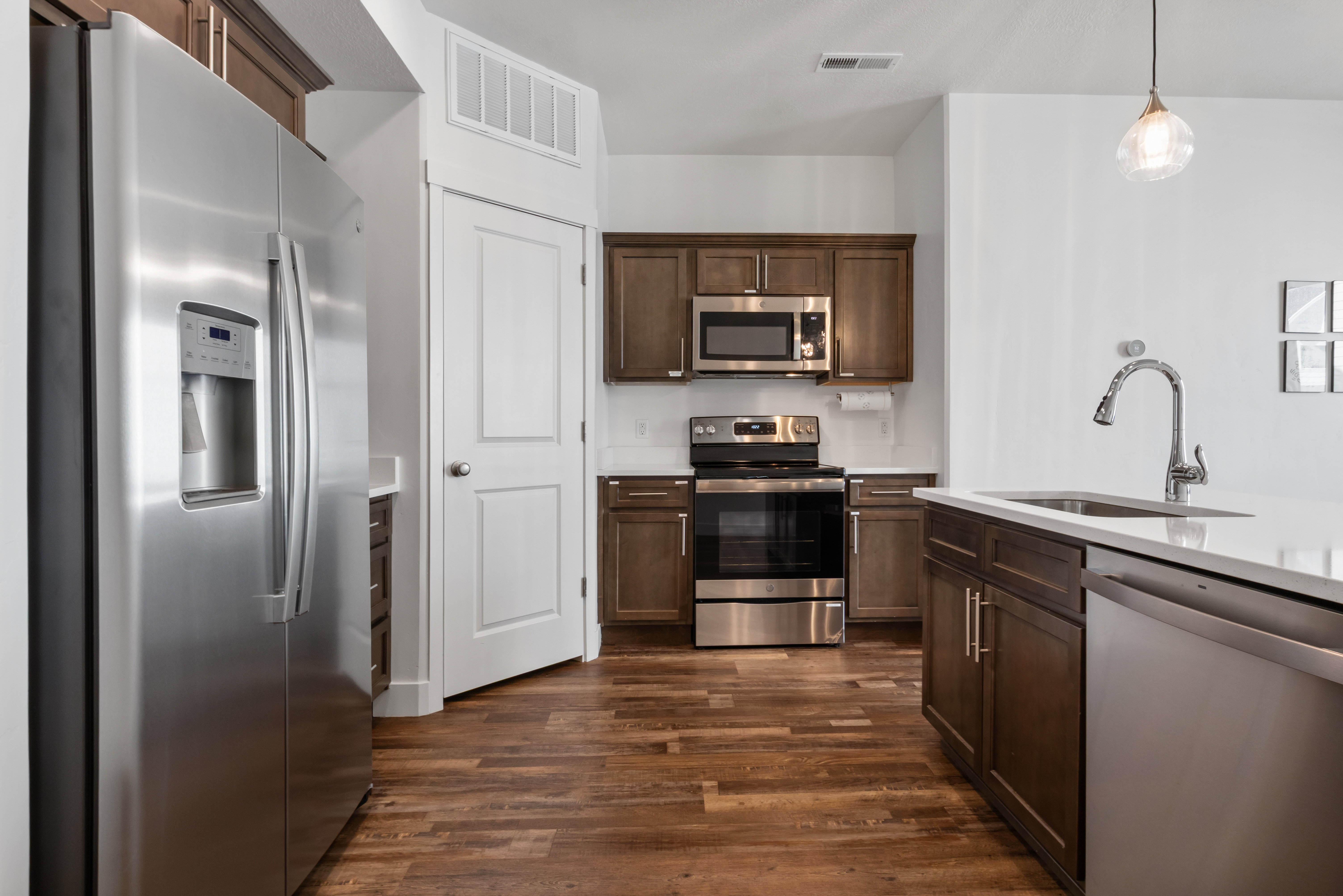 Kitchen featuring wood-finish flooring, stainless steel appliances, dark wood cabinetry, white countertops, and a white subway tile backsplash