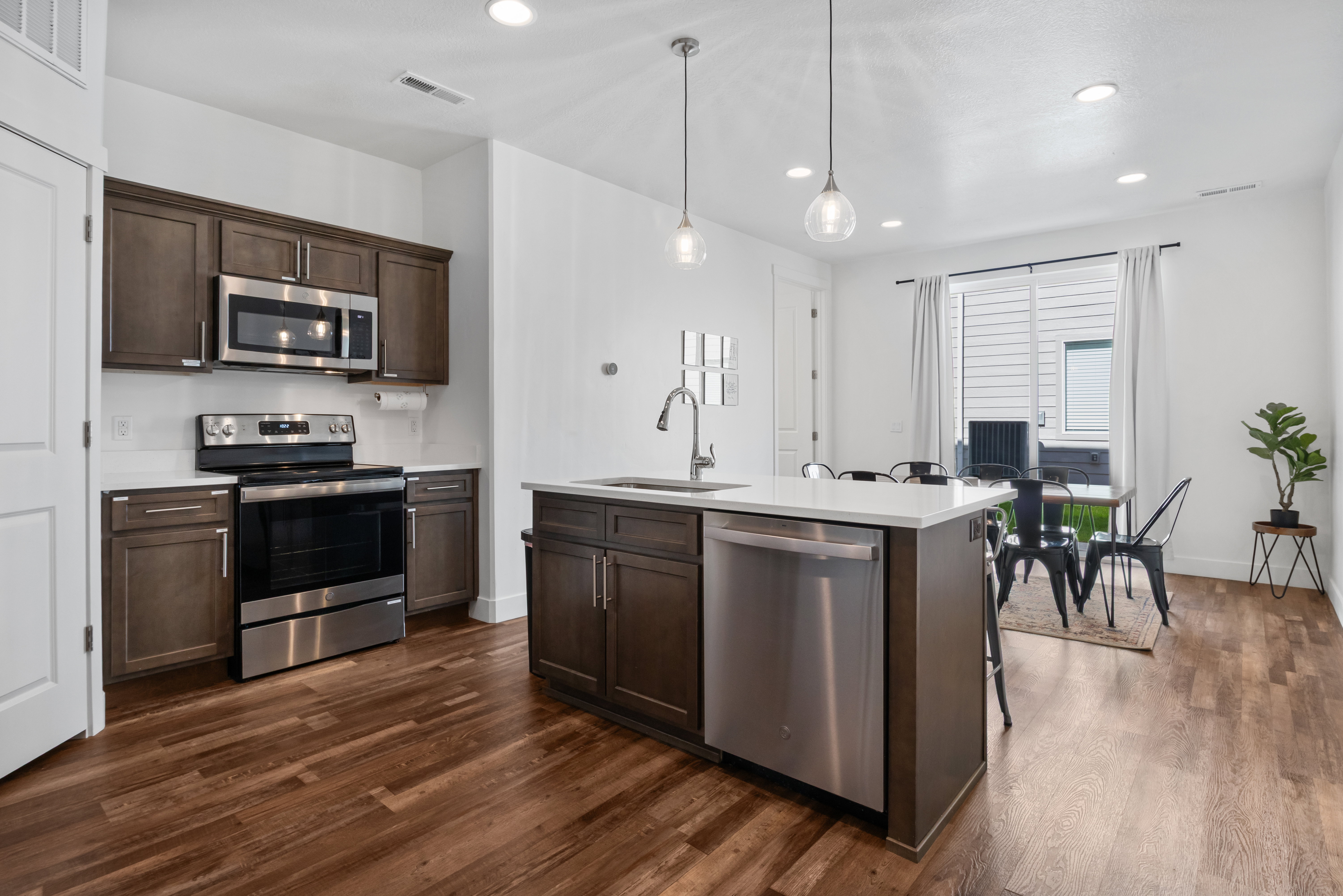 Open-concept kitchen featuring wood-finish flooring, stainless steel appliances, dark wood cabinetry, white countertops, and recessed lighting