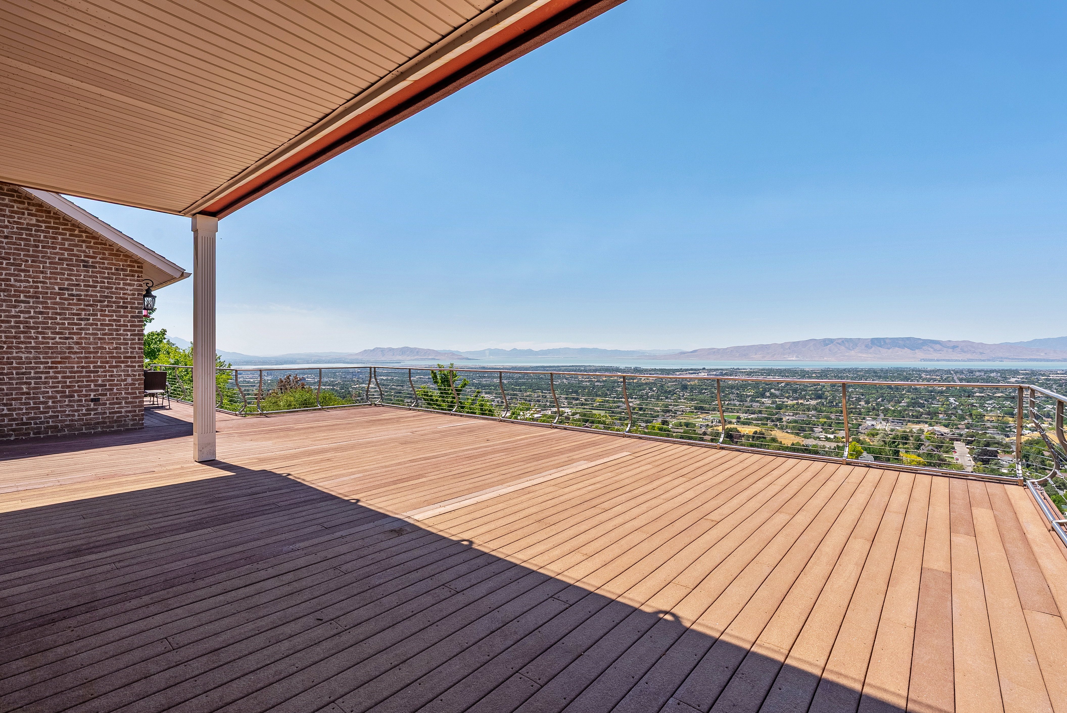 Expansive outdoor deck featuring wood-finish flooring, a contemporary cable railing system, and a scenic backdrop of distant mountains and a body of water