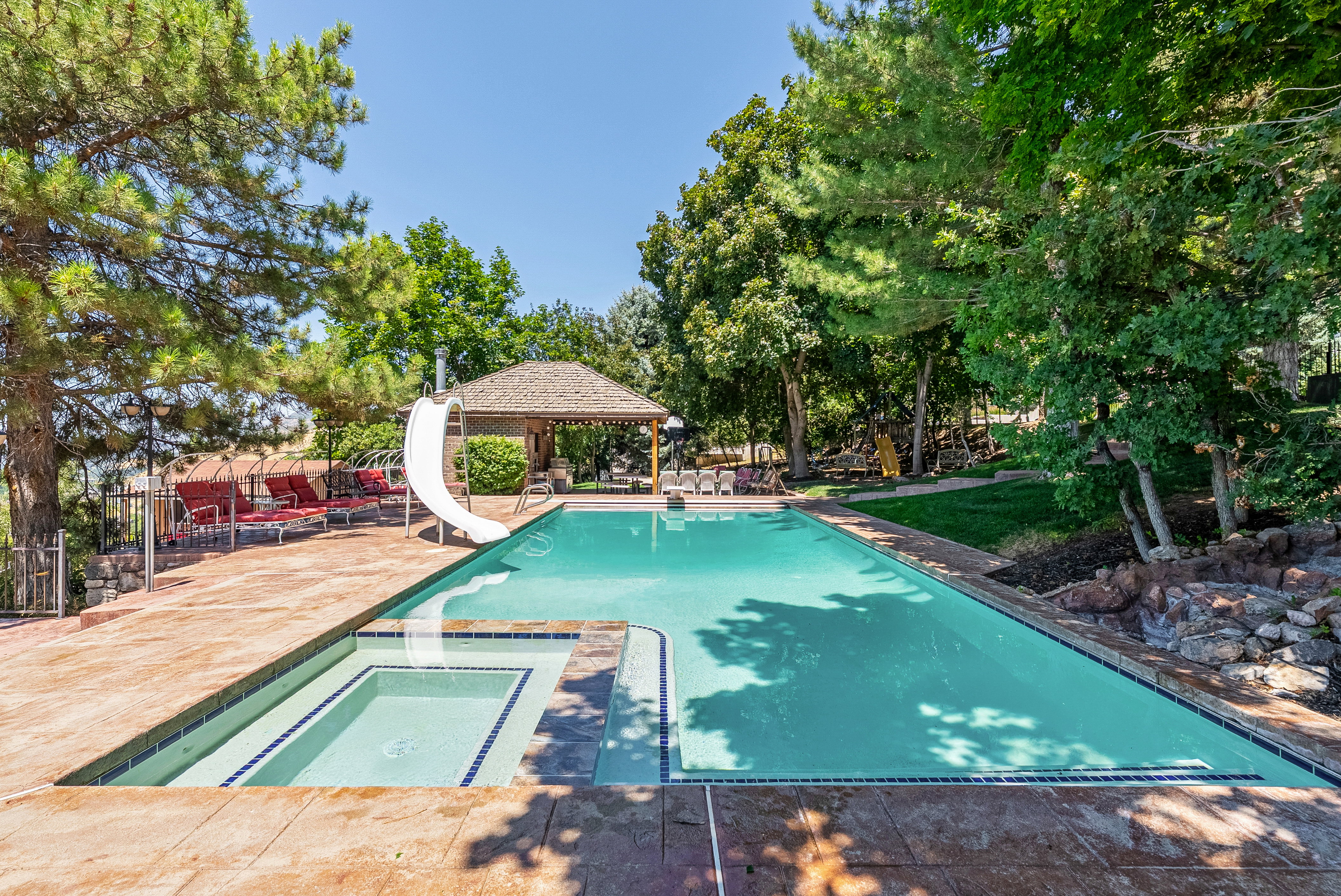 Rectangular swimming pool featuring an integrated spa, an attached slide, and a surrounding paver patio