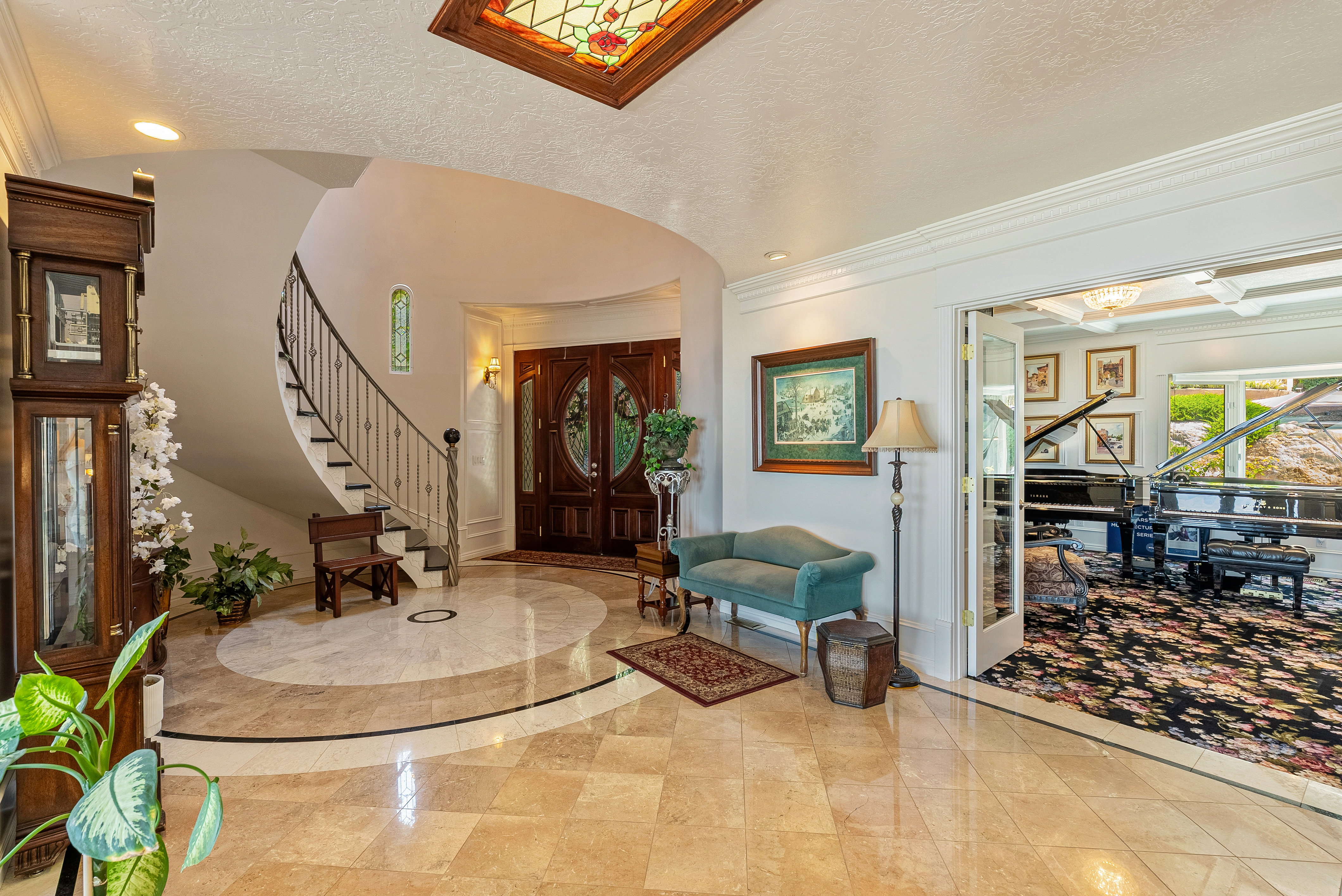 Grand foyer featuring a curved staircase with wrought iron railing, double-door entry, a patterned tile floor, and a stained-glass ceiling insert