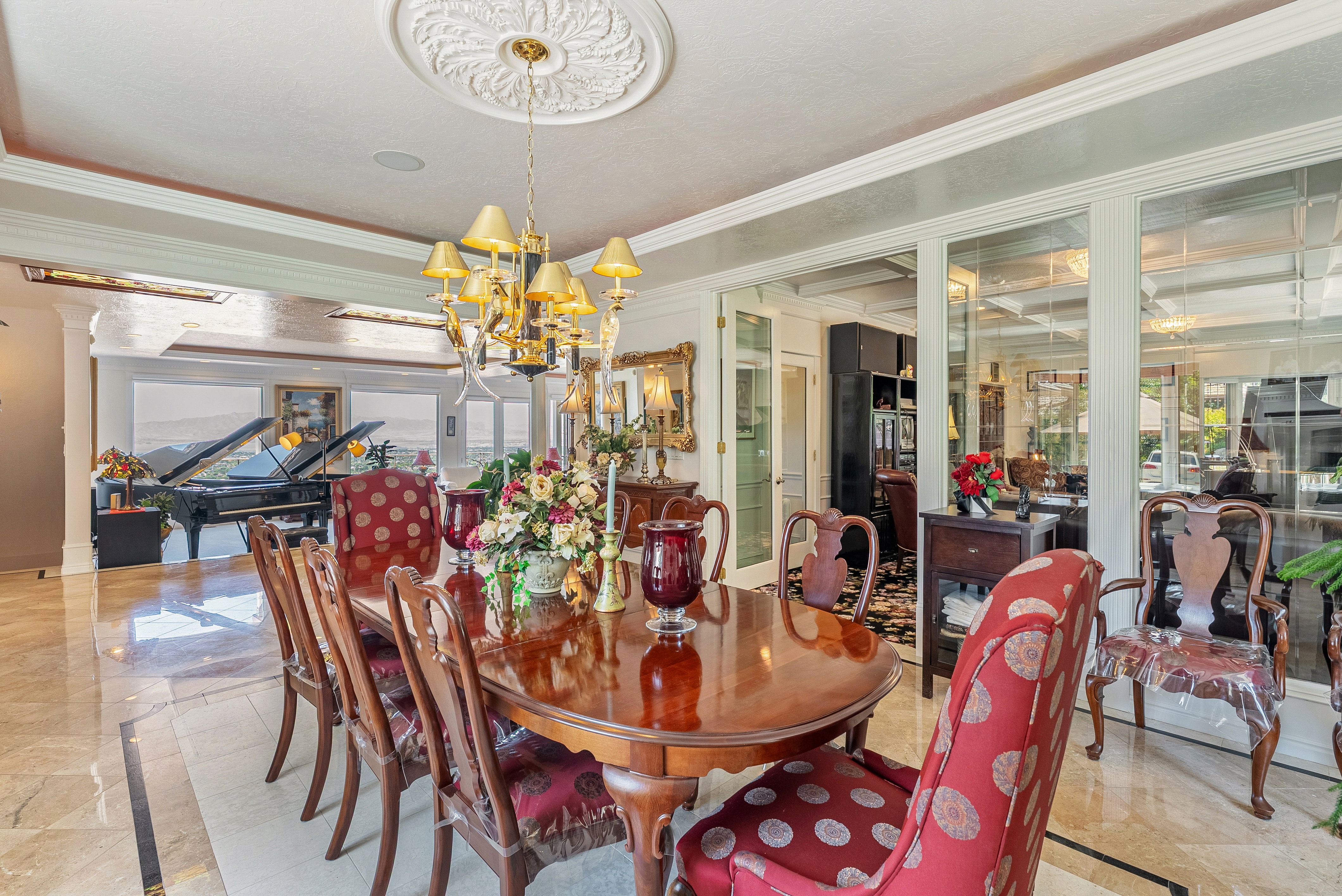 Formal dining area featuring a prominent chandelier with a decorative ceiling medallion, extensive crown molding, and large format polished tile flooring