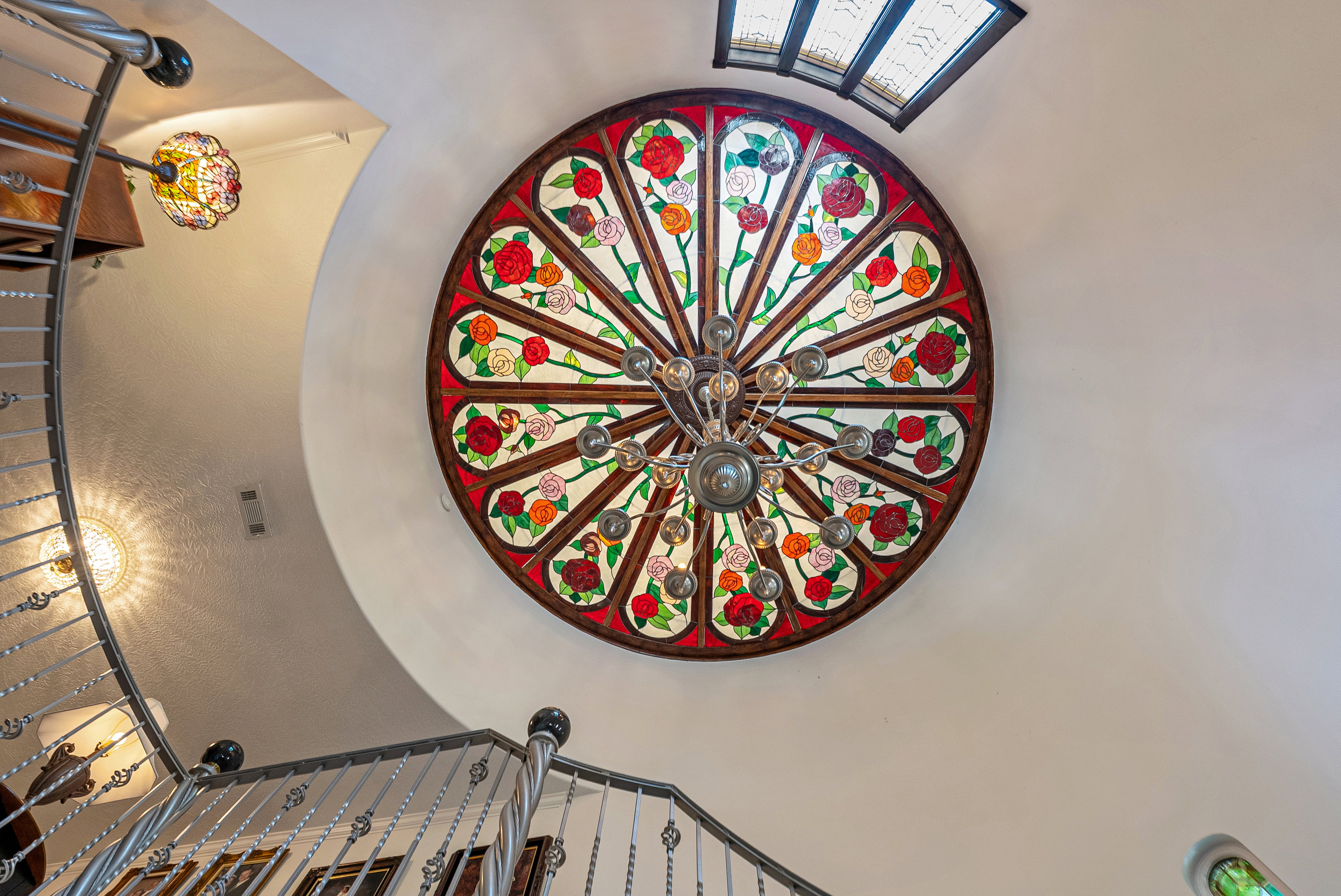 Circular stained glass ceiling fixture with a central chandelier, showcasing floral motifs