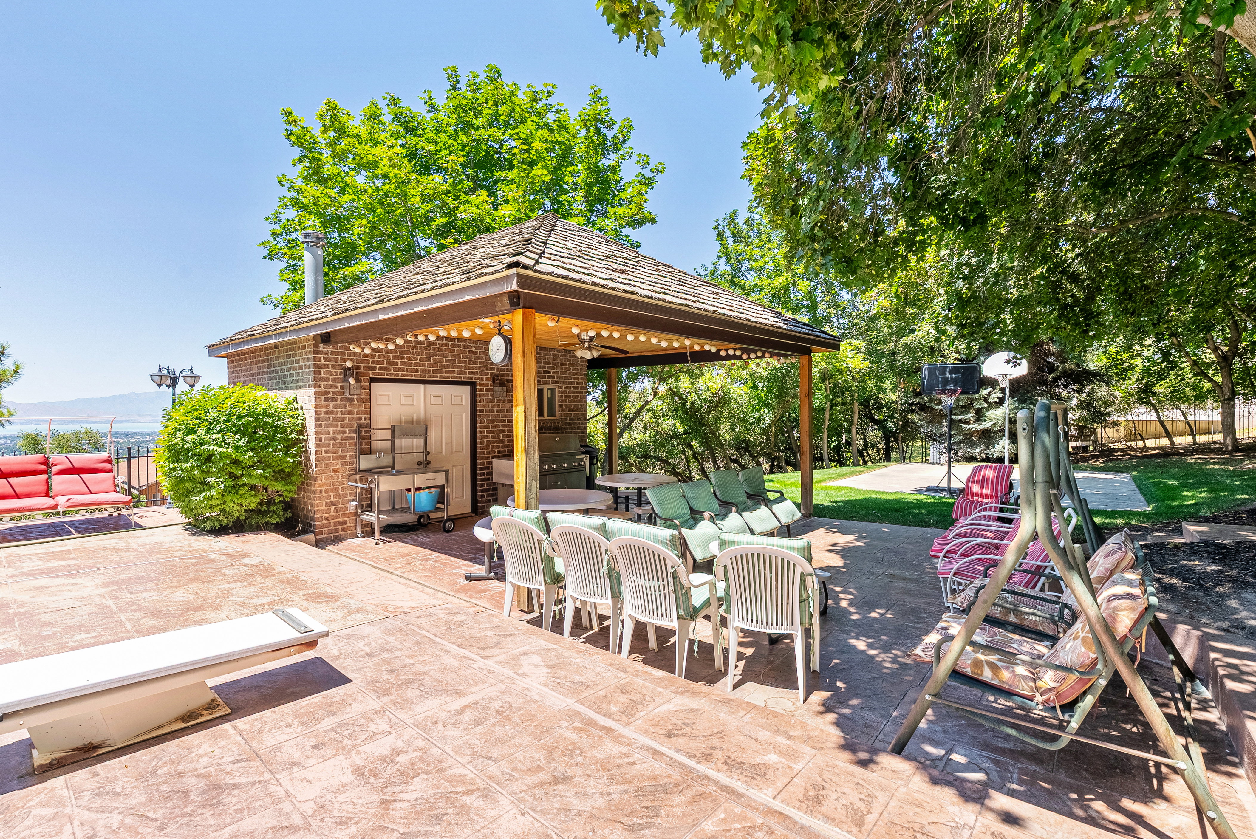 Expansive stamped concrete patio featuring a brick-built outdoor kitchen structure with a covered dining area, string lighting, and mature landscaping
