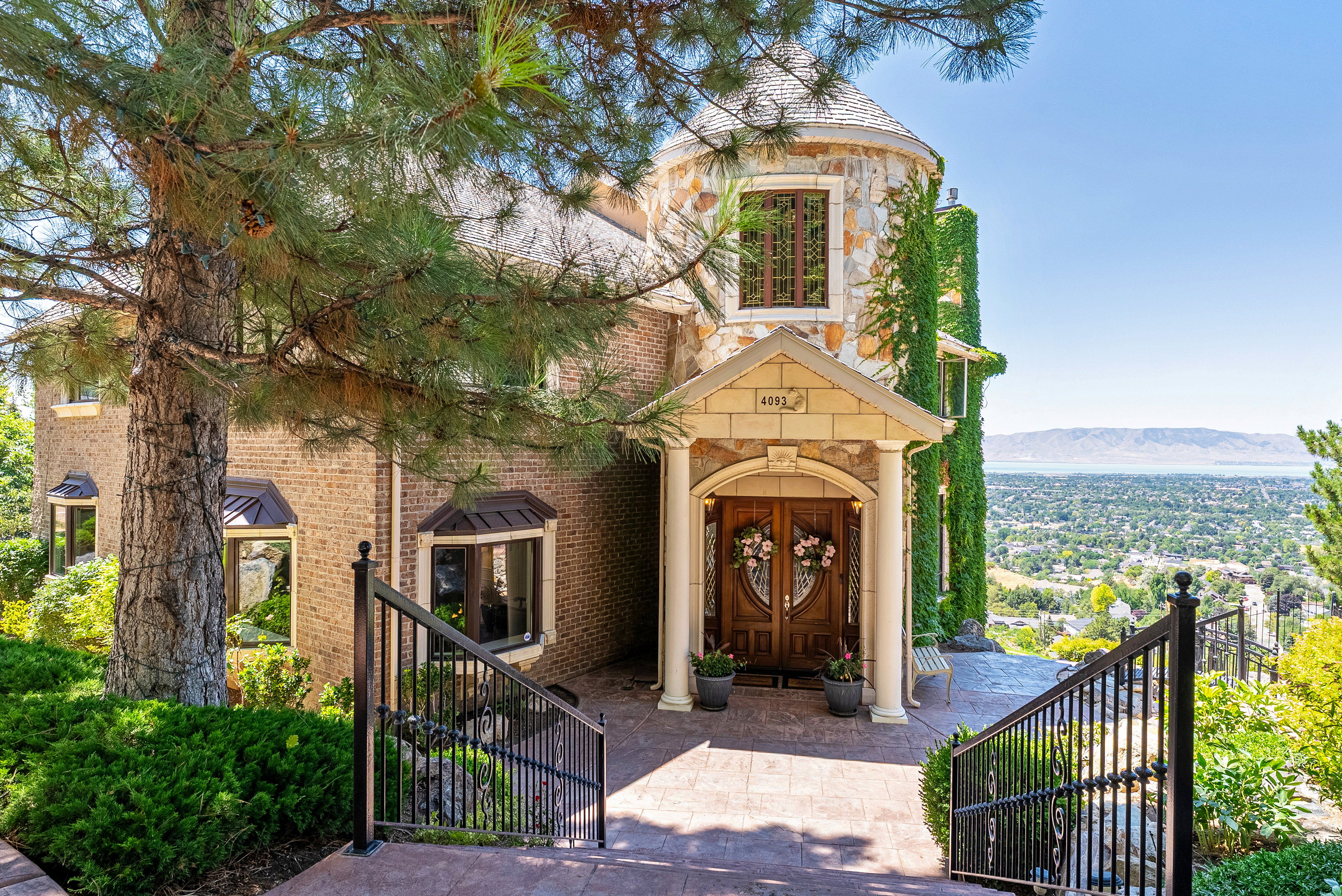Stone and brick facade featuring a turret, mature landscaping, and a wood-finish double entry door