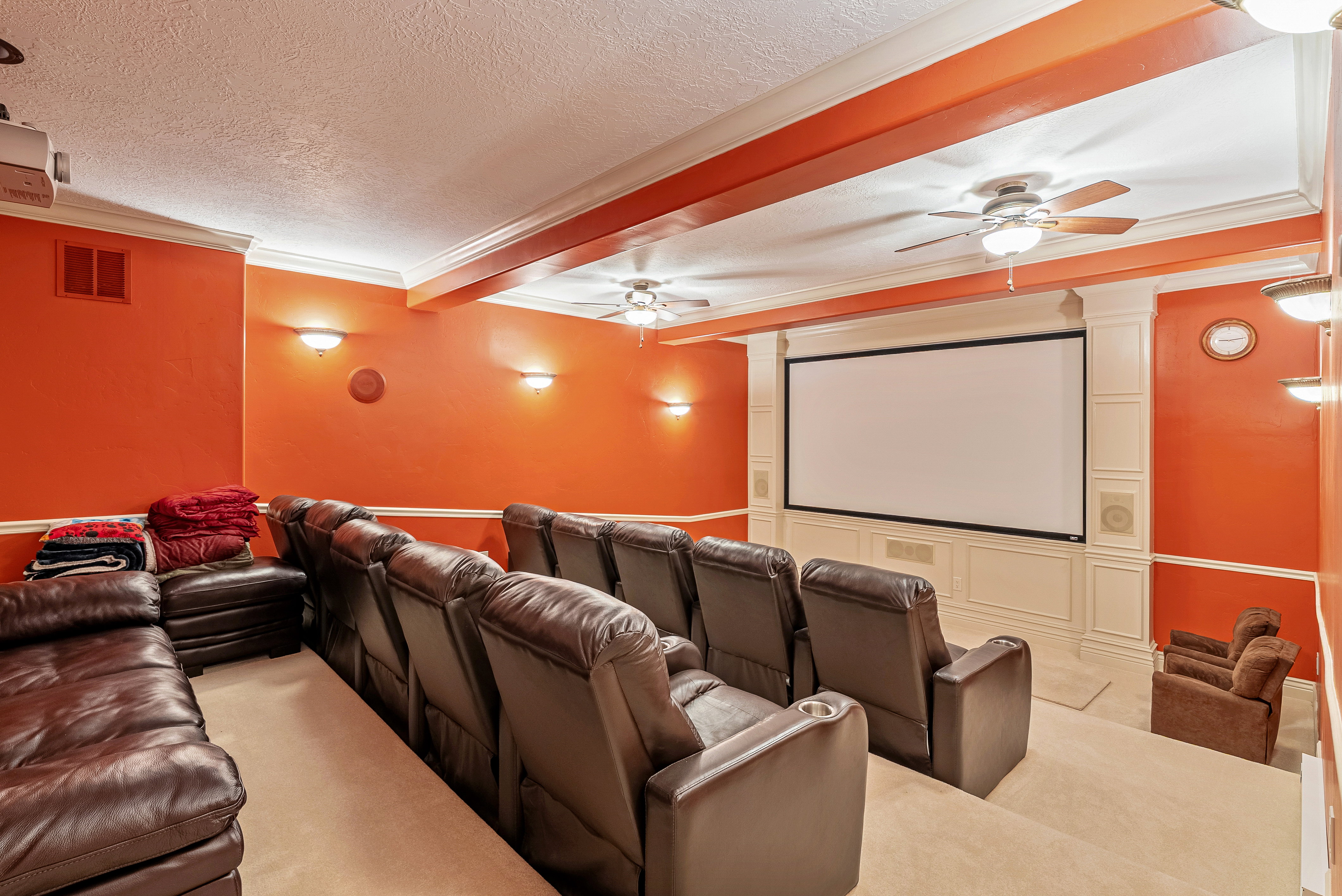 Dedicated home theater featuring a large projection screen, coffered ceiling, ceiling fans, wall sconces, and tiered seating