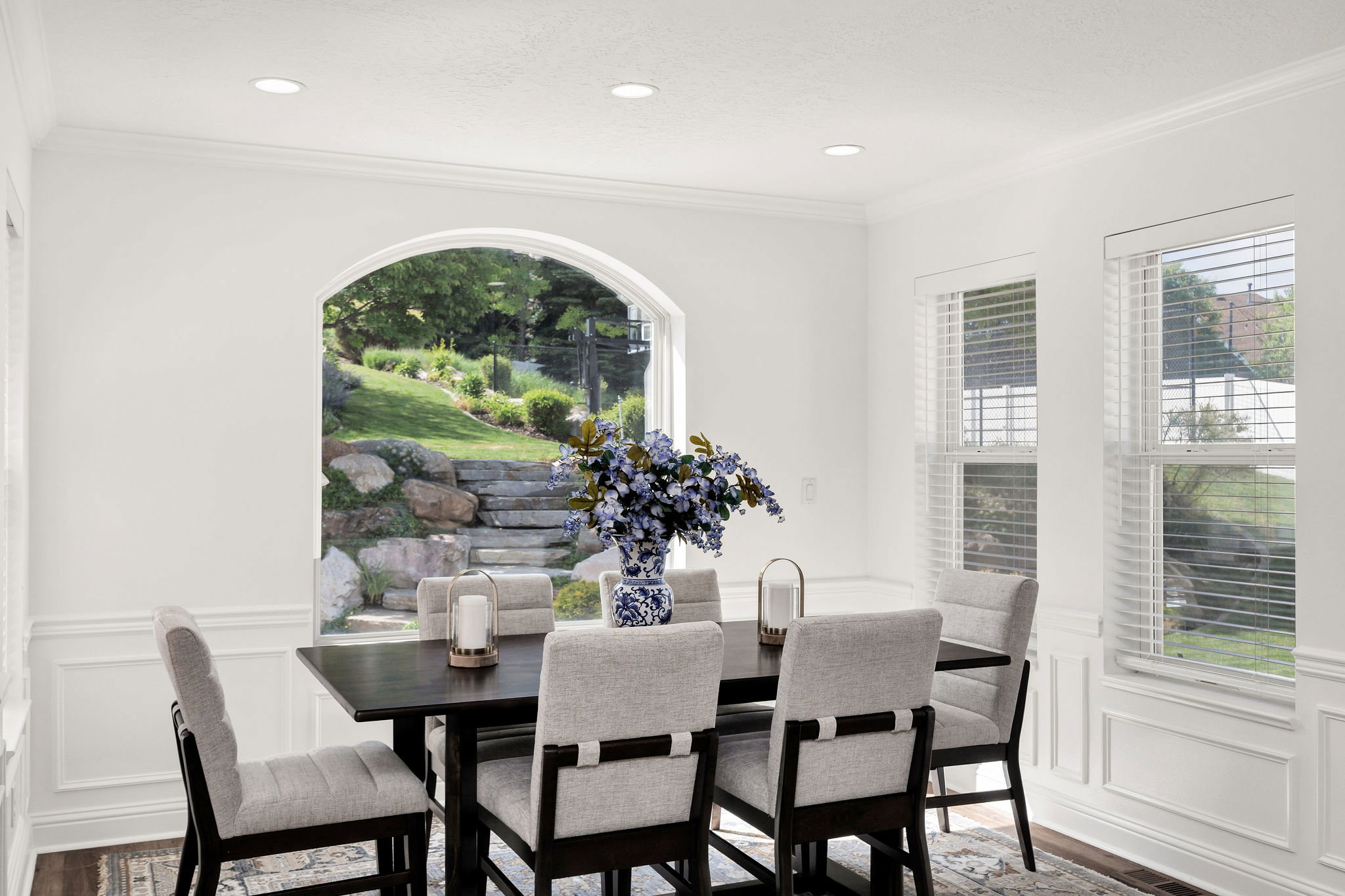 Bright dining area featuring a prominent arched window, recessed lighting, crown molding, and wainscoting