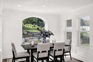 Bright dining area featuring a prominent arched window, recessed lighting, crown molding, and wainscoting